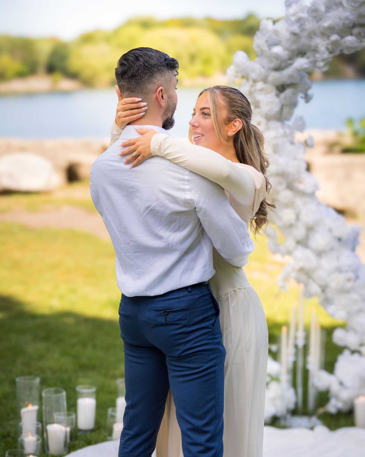 Romantic wedding moment captured under decorative white flower arch with candles.