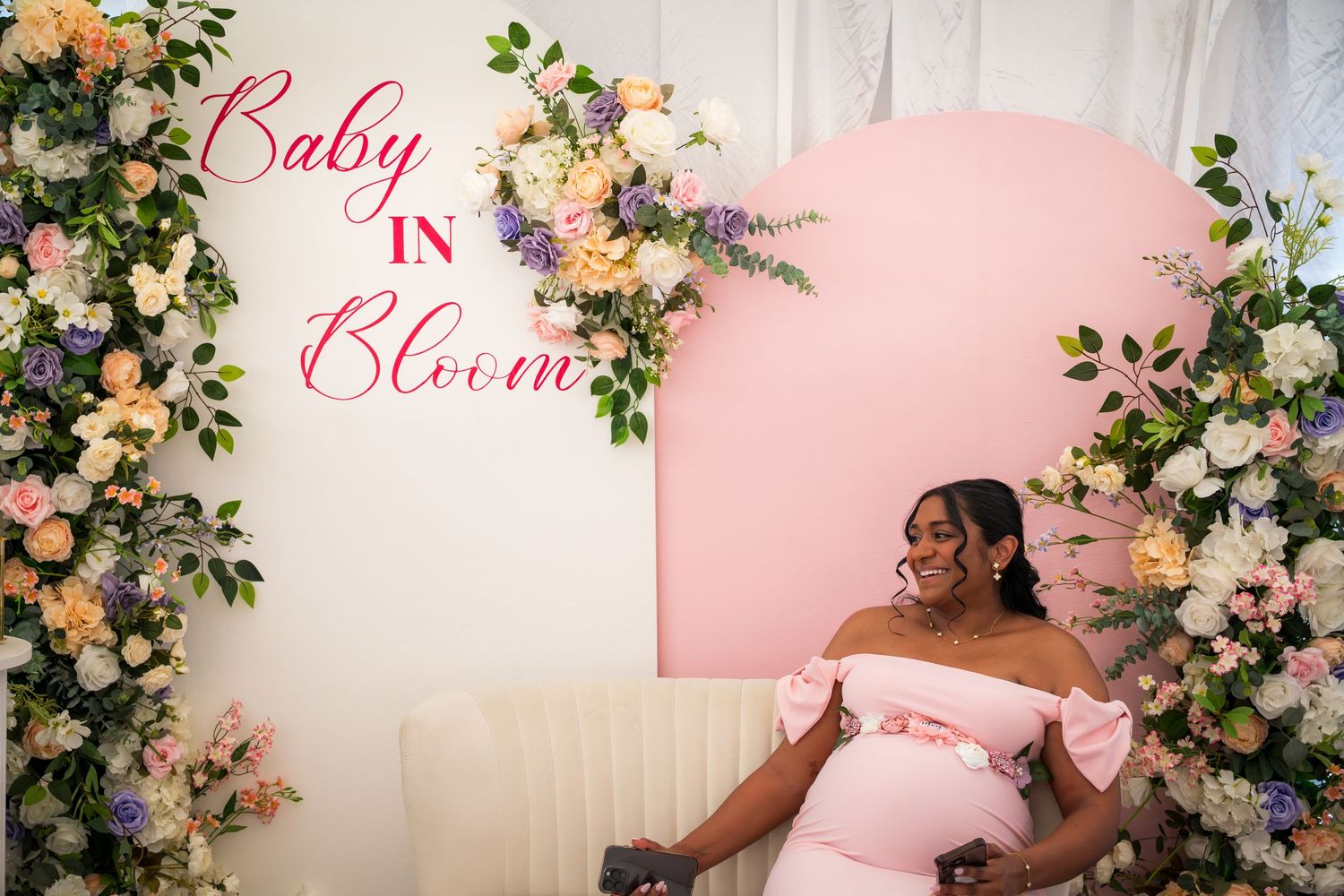 Pink and floral decorated baby shower backdrop with elegant white draping.