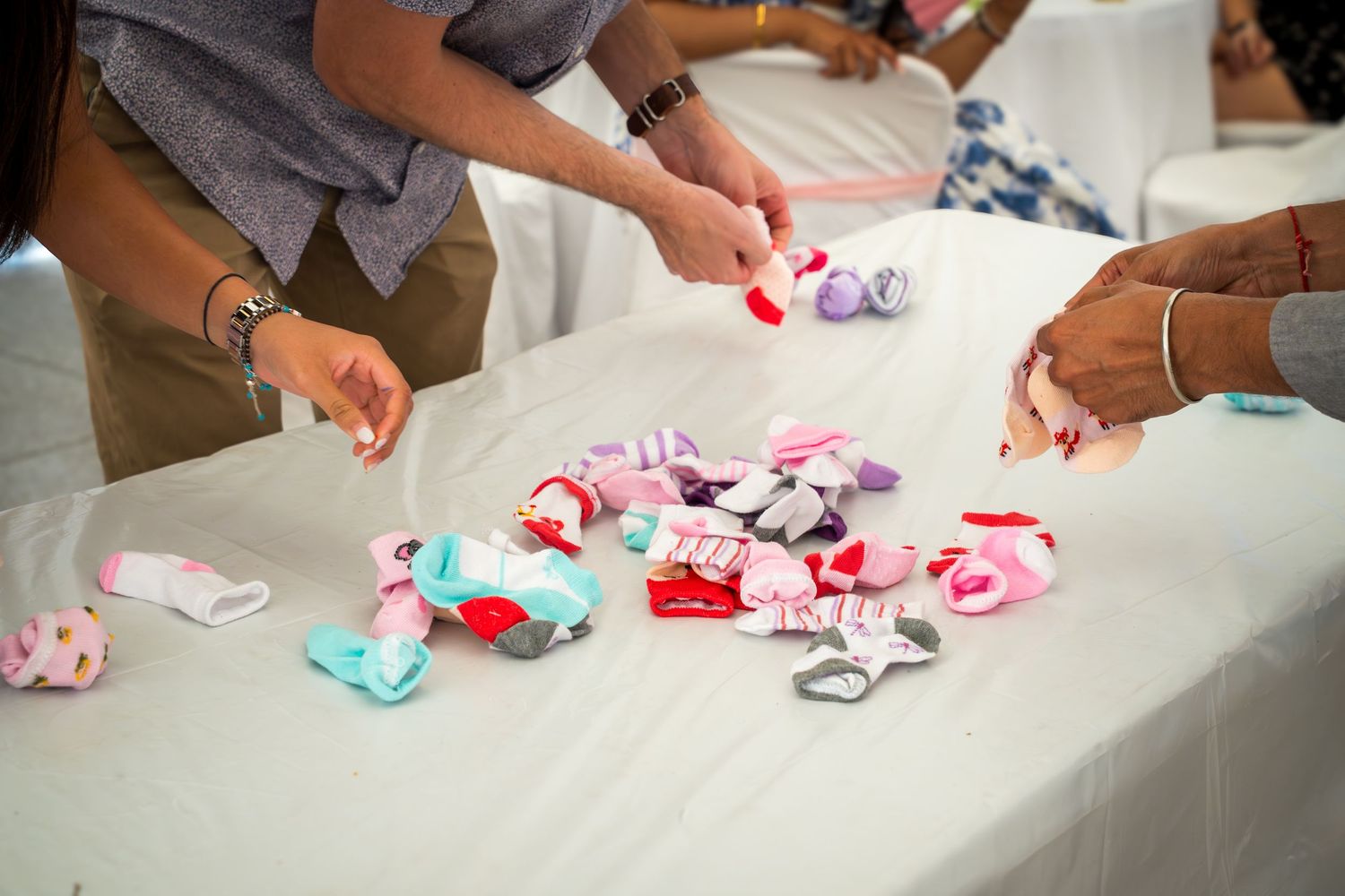 Close-up view of hands arranging pink and teal decorative items on a white surface.