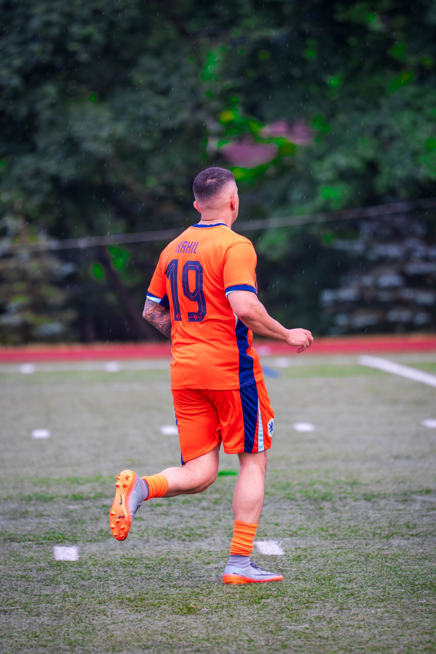 Soccer player in bright orange uniform practicing kicking technique on field.