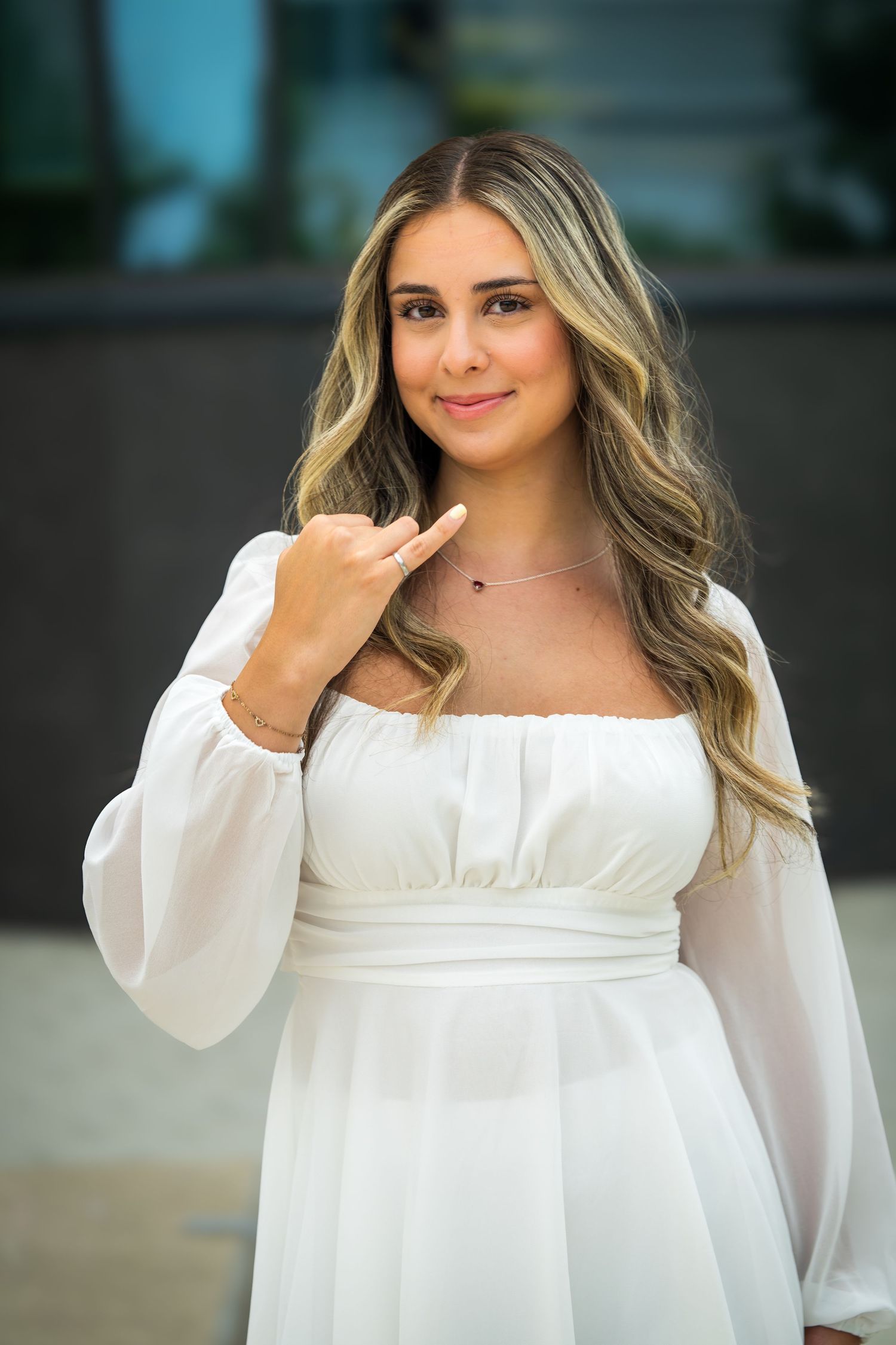 Graduate in ethereal white dress gestures while posing for graduation photos.