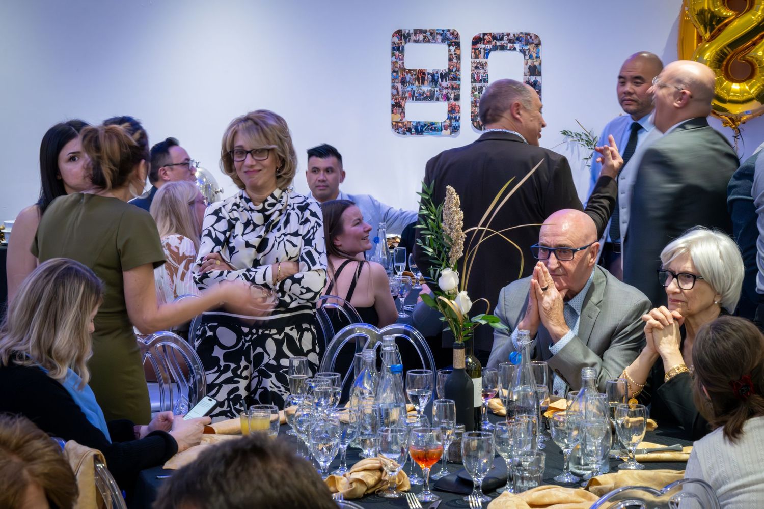 A festive party scene with gold balloons and people gathered around tables.