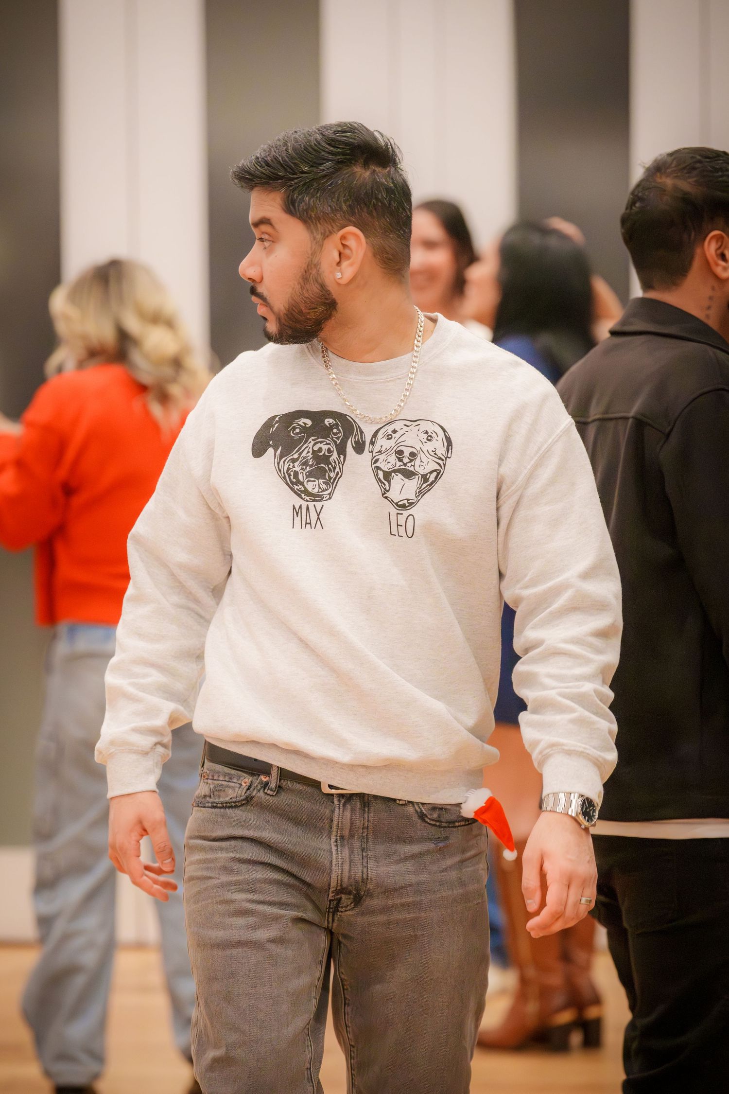 Person wearing graphic sweatshirt with cartoon faces at indoor social gathering.
