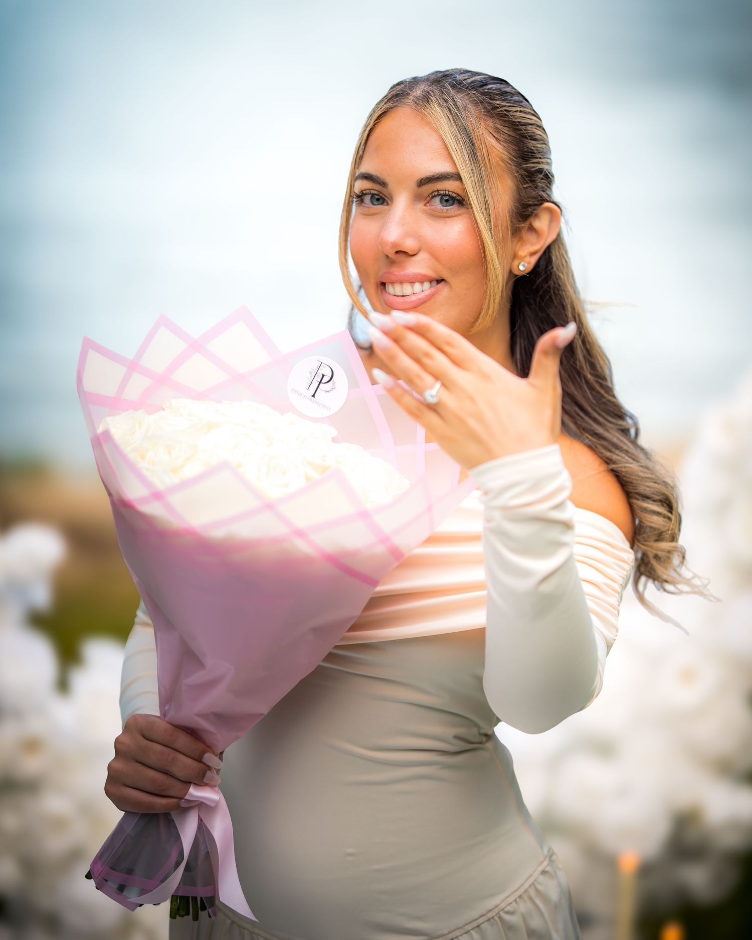 Person in off-shoulder dress poses with white flower bouquet while touching their face.