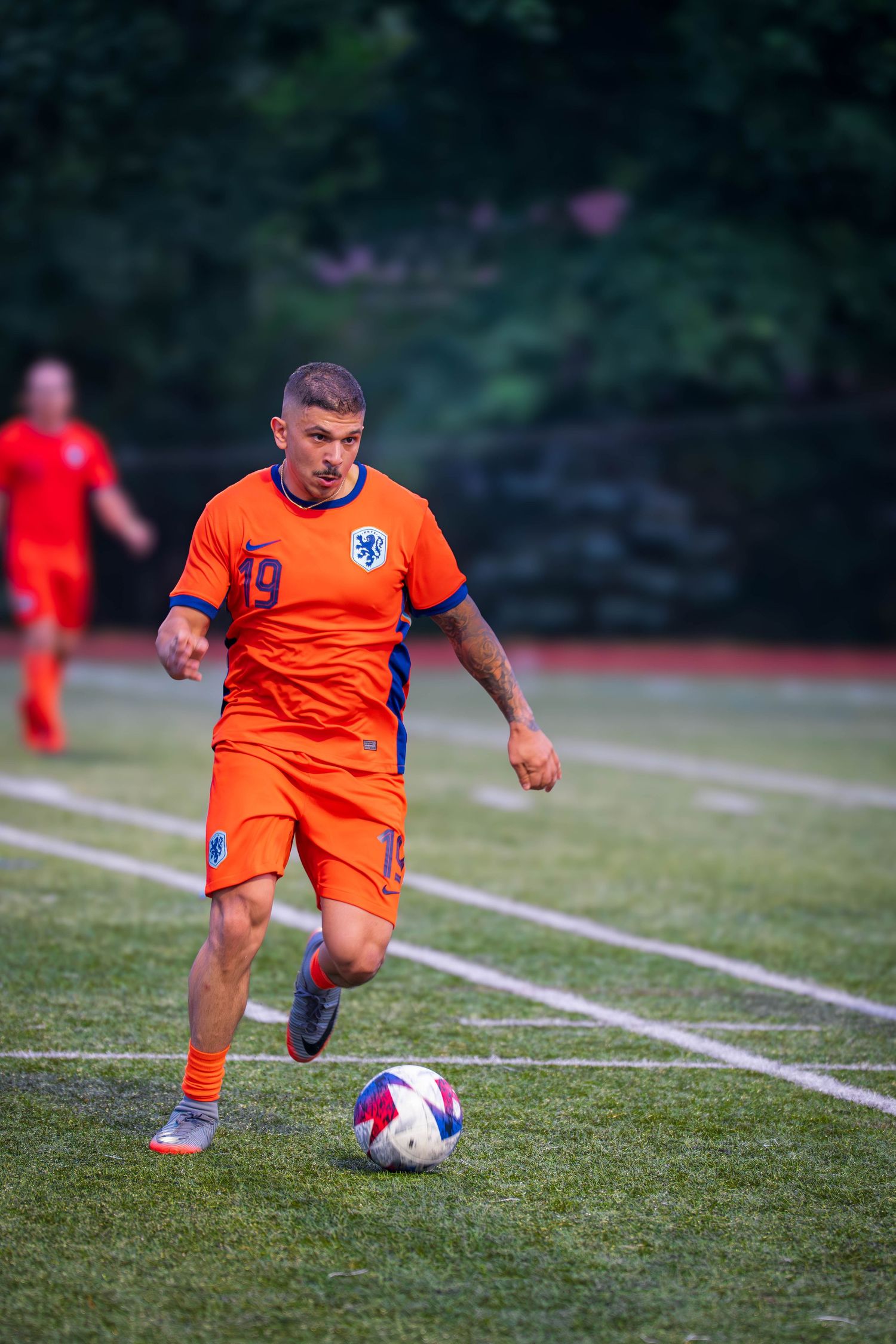 Player in bright orange uniform controls soccer ball during match on outdoor field.