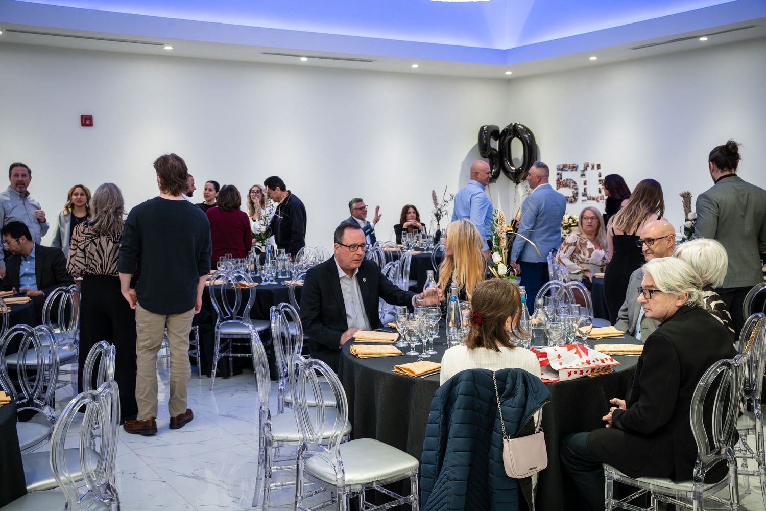 Reception area with clear ghost chairs and guests gathering around tables.