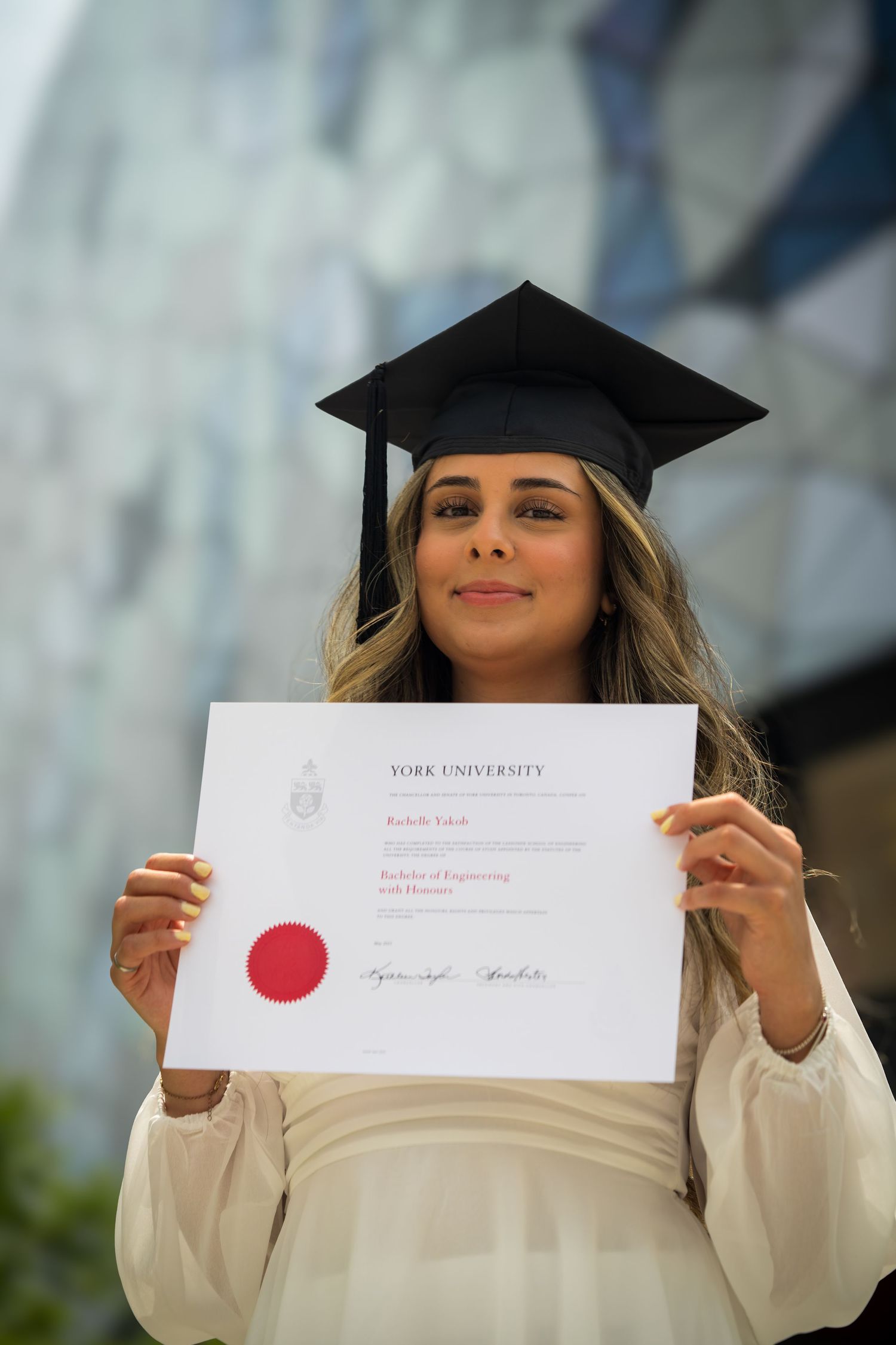 Graduate shows off official York University diploma in outdoor setting.