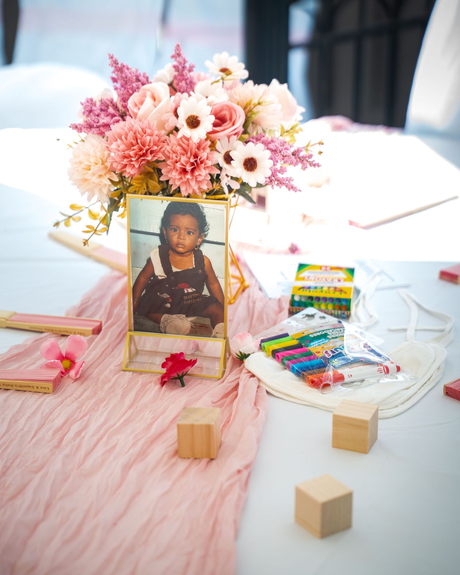 Baby shower activity table with pink decor, flowers, and framed photographs.