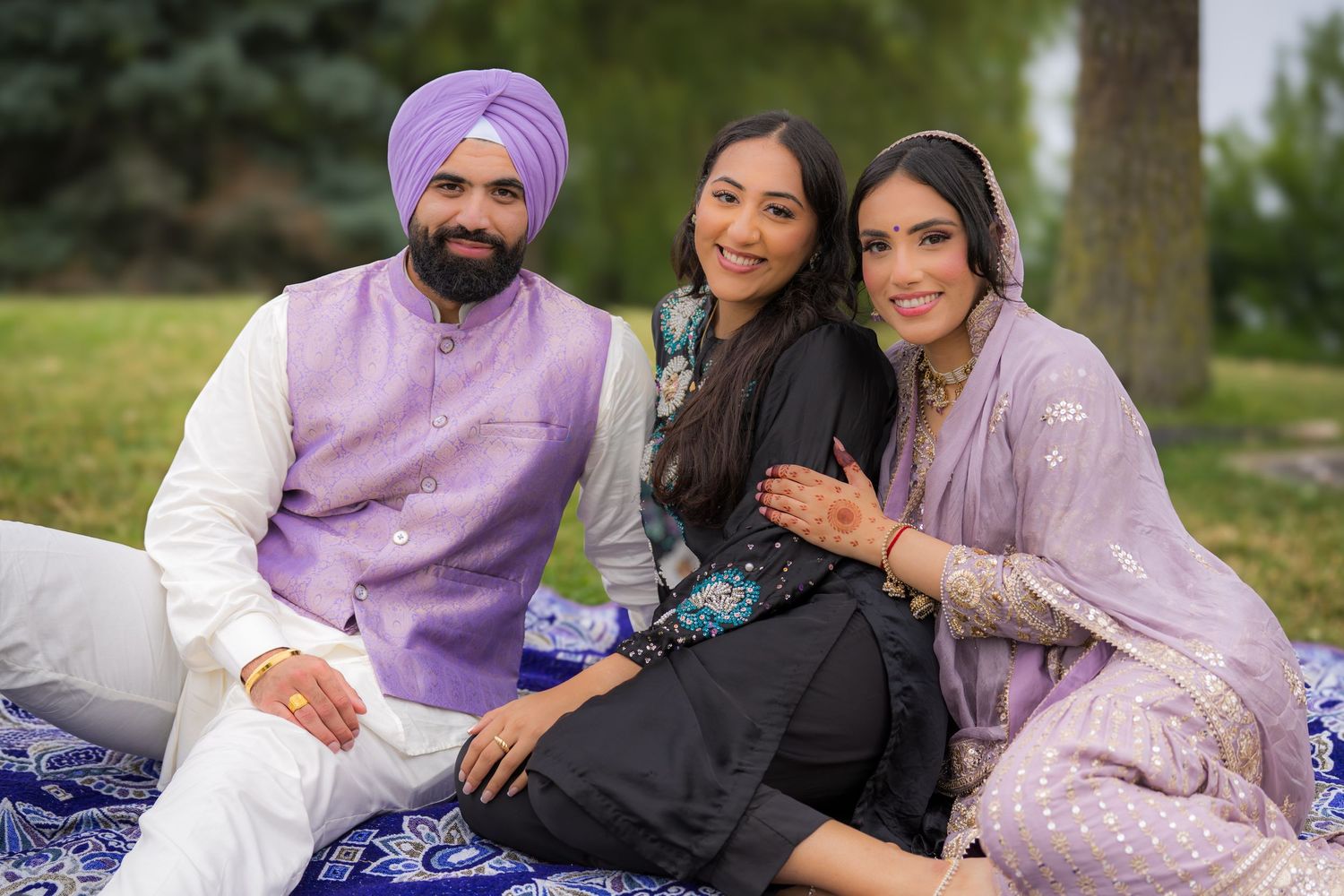 A family group lounges on a blue patterned blanket in a park setting wearing coordinated traditional clothing.
