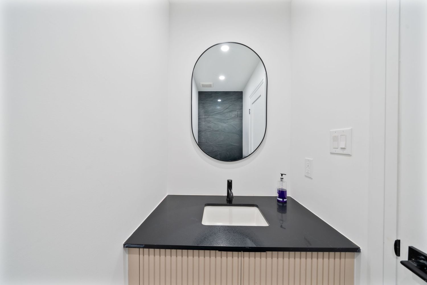 Modern bathroom interior with black countertop, round mirror, and white walls featuring minimalist design elements.