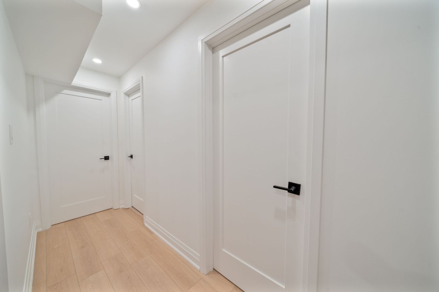 A modern white interior hallway with paneled walls and multiple doorways leading to different rooms.