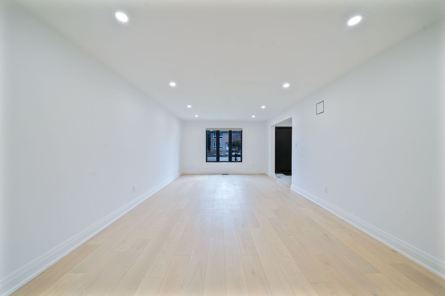 Modern white hallway with recessed lighting and light hardwood flooring leading to a bright window at the end.