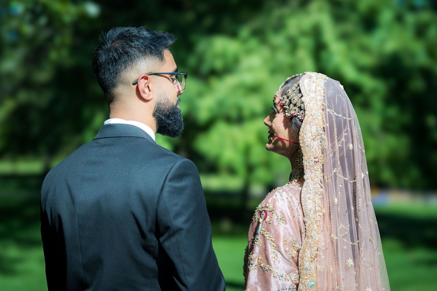 Couple in traditional South Asian wedding attire standing together in a lush garden setting.