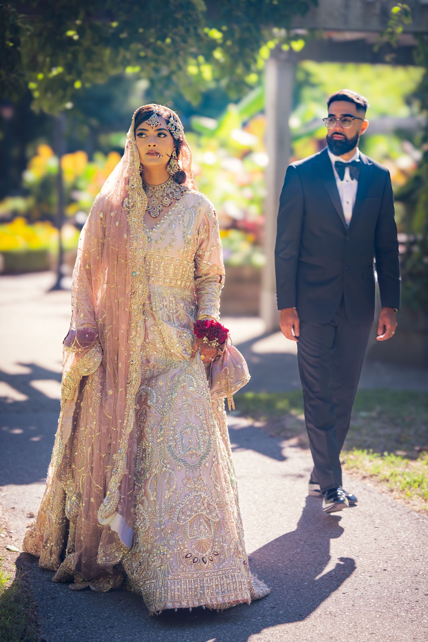 Wedding couple walking outdoors, bride wearing an intricately detailed peach gown with matching veil.