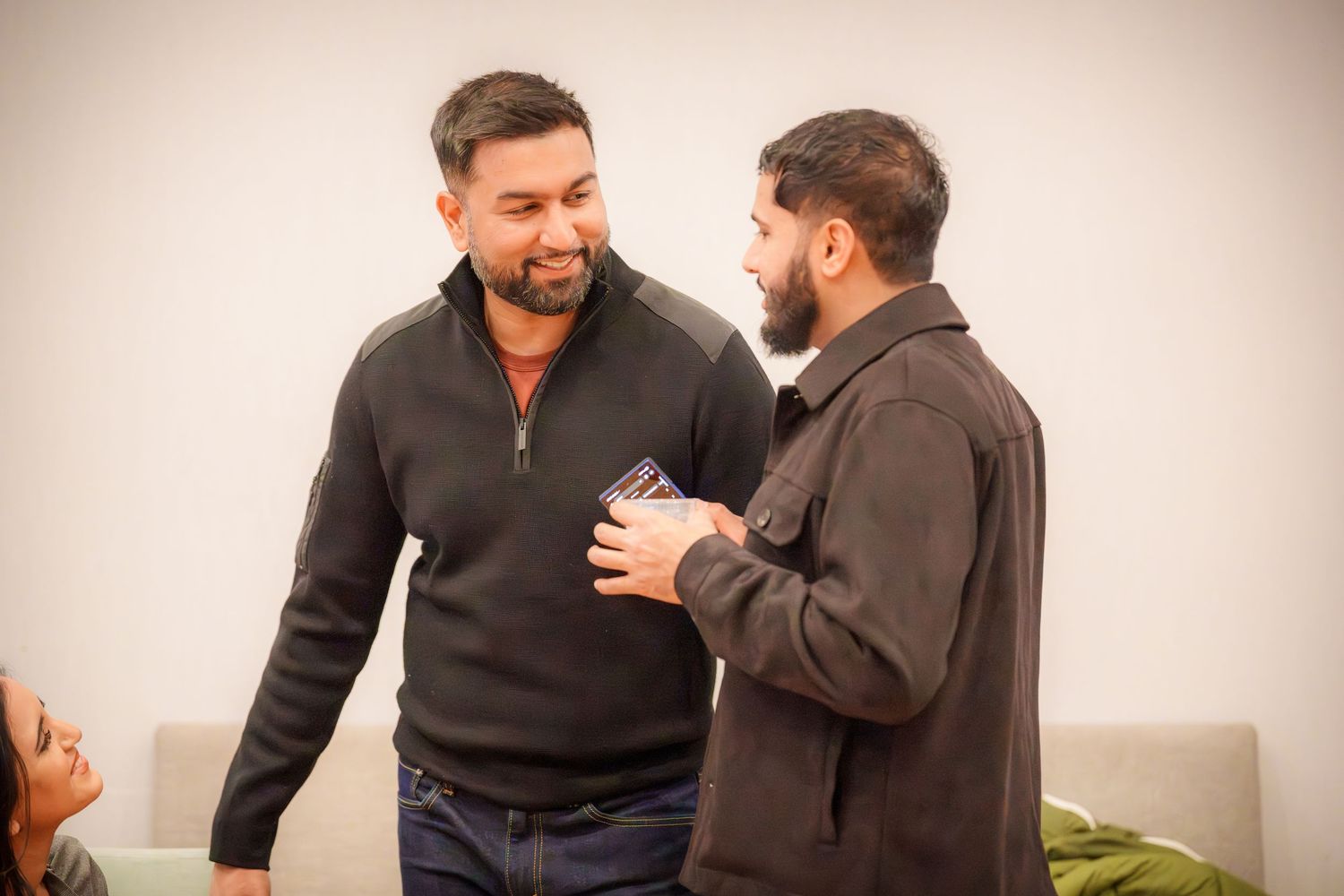 Two people in dark sweaters having an animated conversation at an indoor gathering.