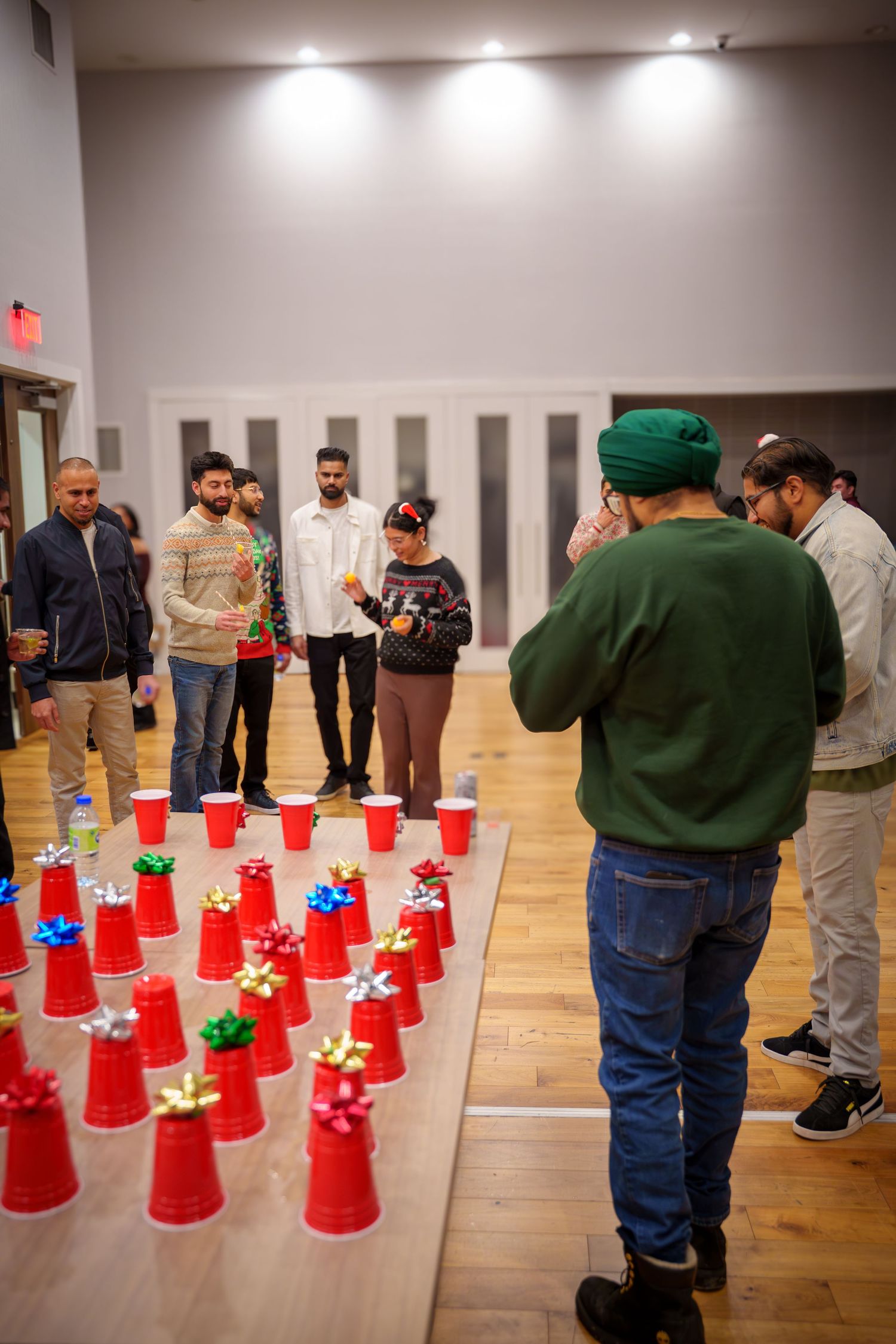 Group of people observing red and green cups arranged on wooden floor during indoor event.