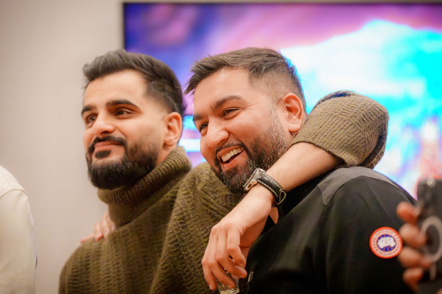 Two friends sharing a laugh and embracing at an indoor party.