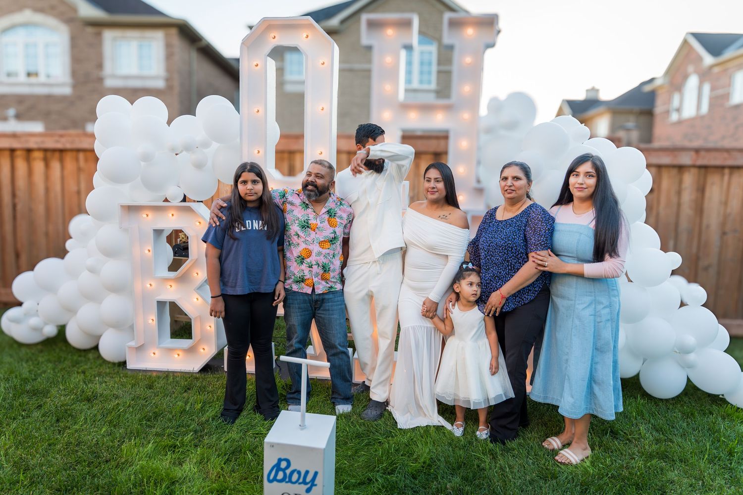 Family group photo at gender reveal party with illuminated OH BABY sign and white balloons.