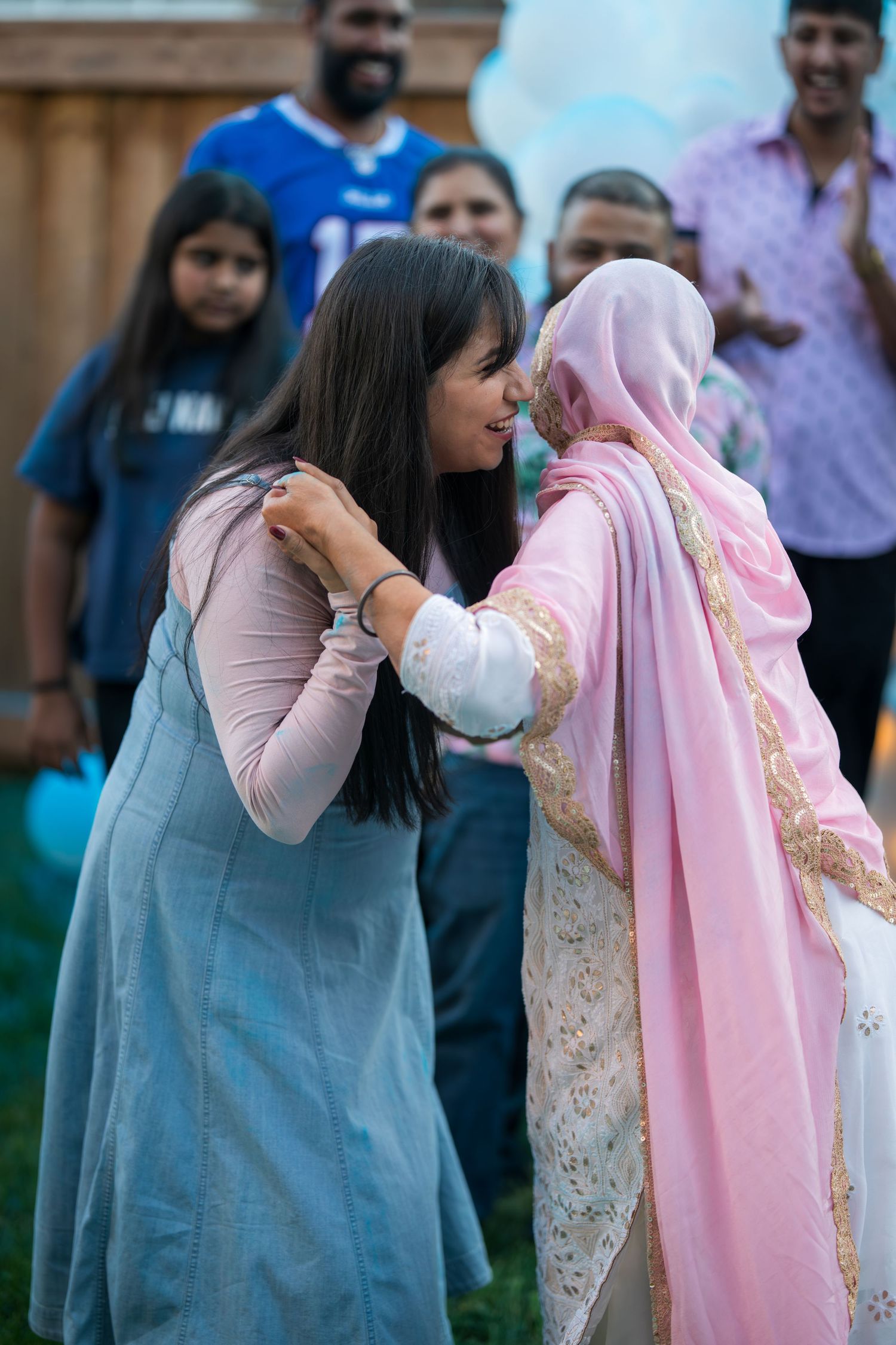 Two women share a tender forehead touch greeting at an outdoor South Asian family gathering.