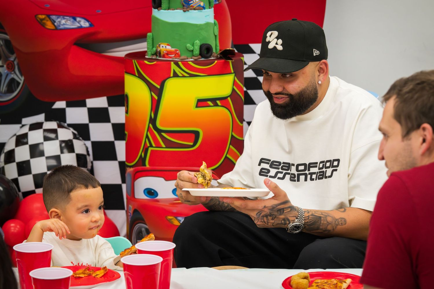 Man in Fear of God Essentials tee serving food to a child at Cars themed birthday party.