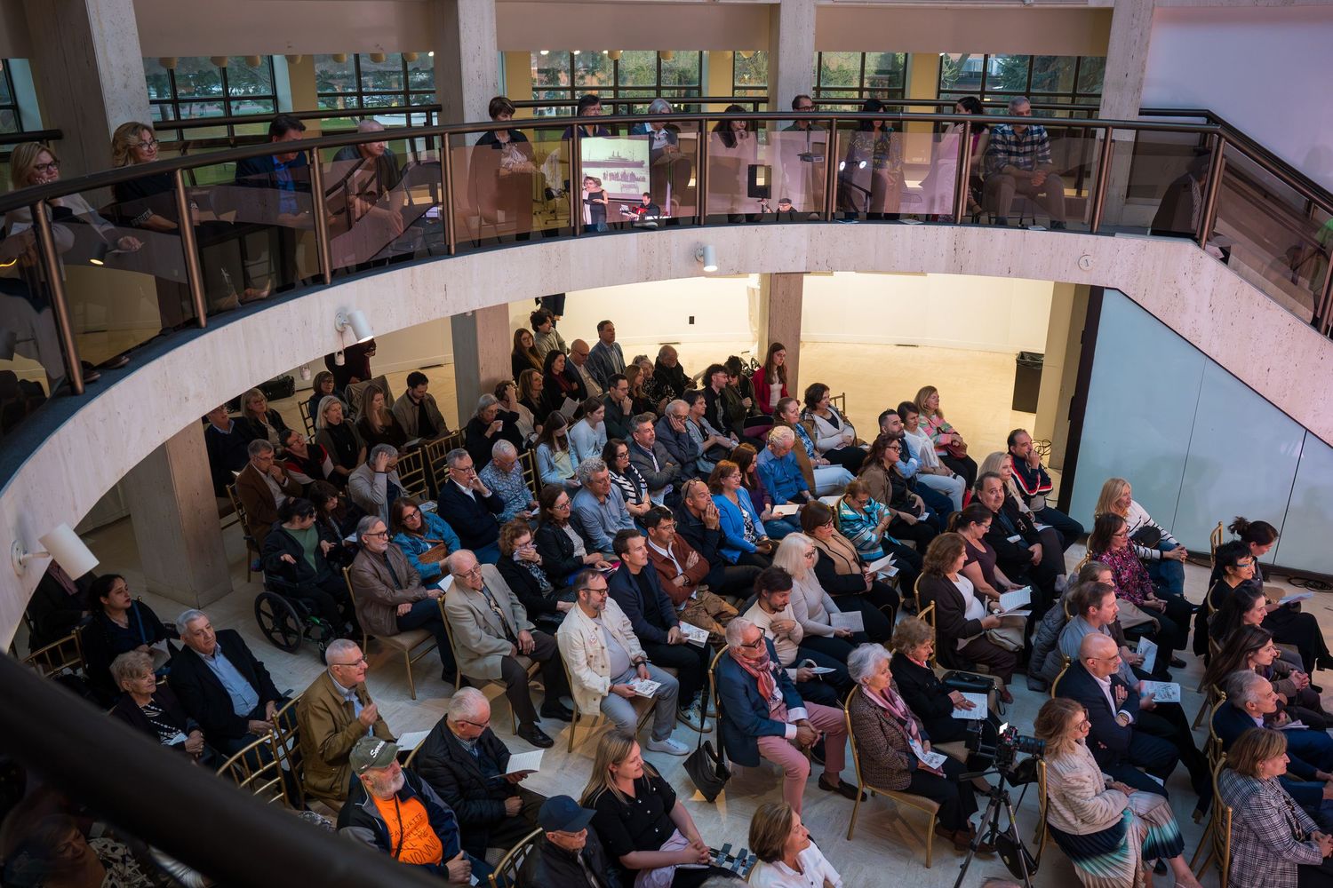 Aerial view of a large audience gathered in a modern atrium venue for a cultural event or conference.