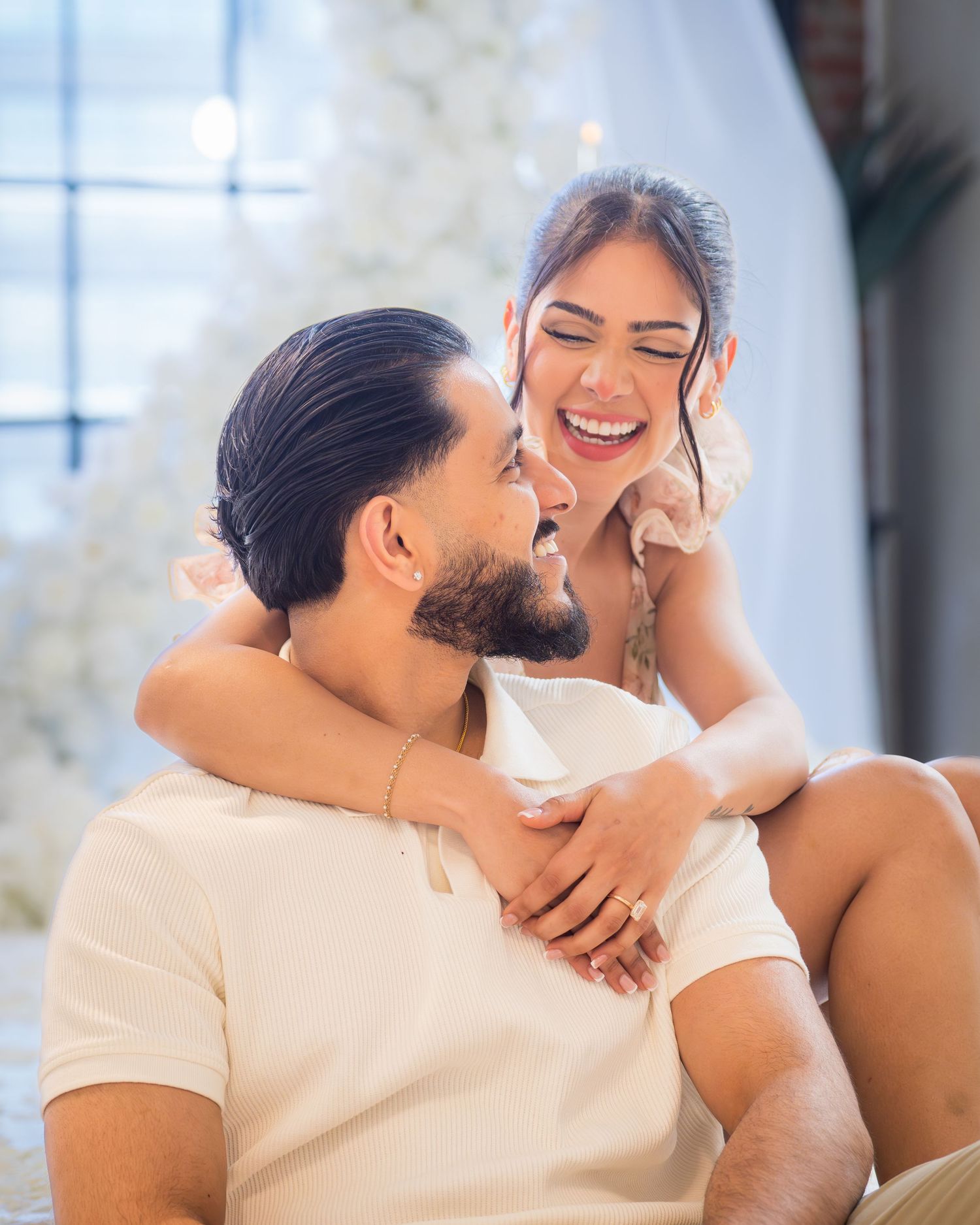A laughing couple shares a joyful embrace seated together in a beautifully decorated proposal venue.
