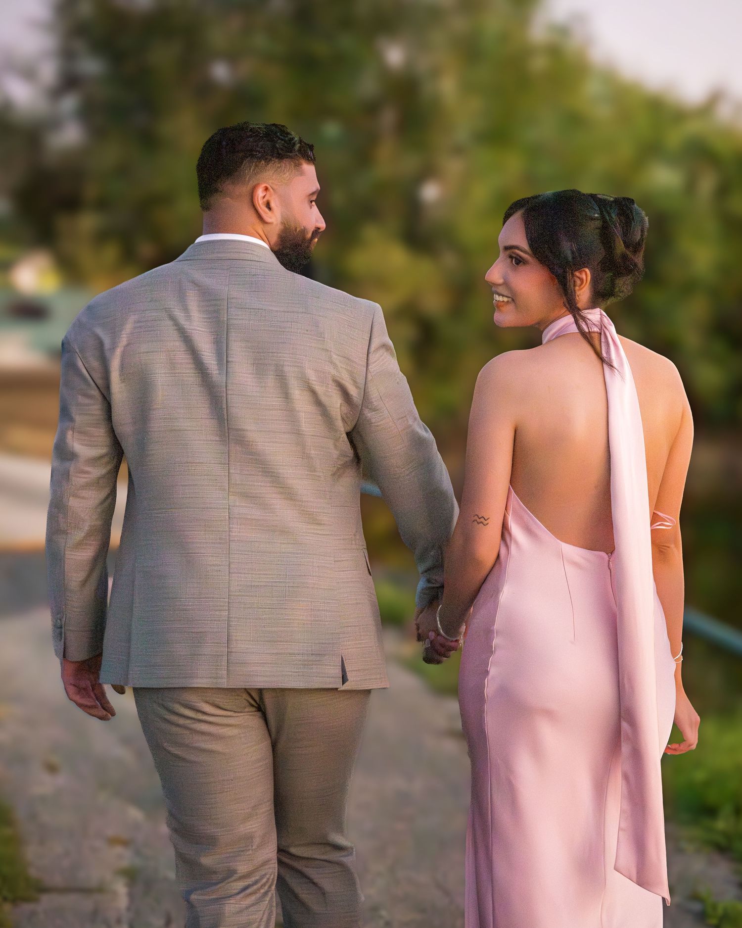 Couple in formal attire walking along scenic outdoor trail.