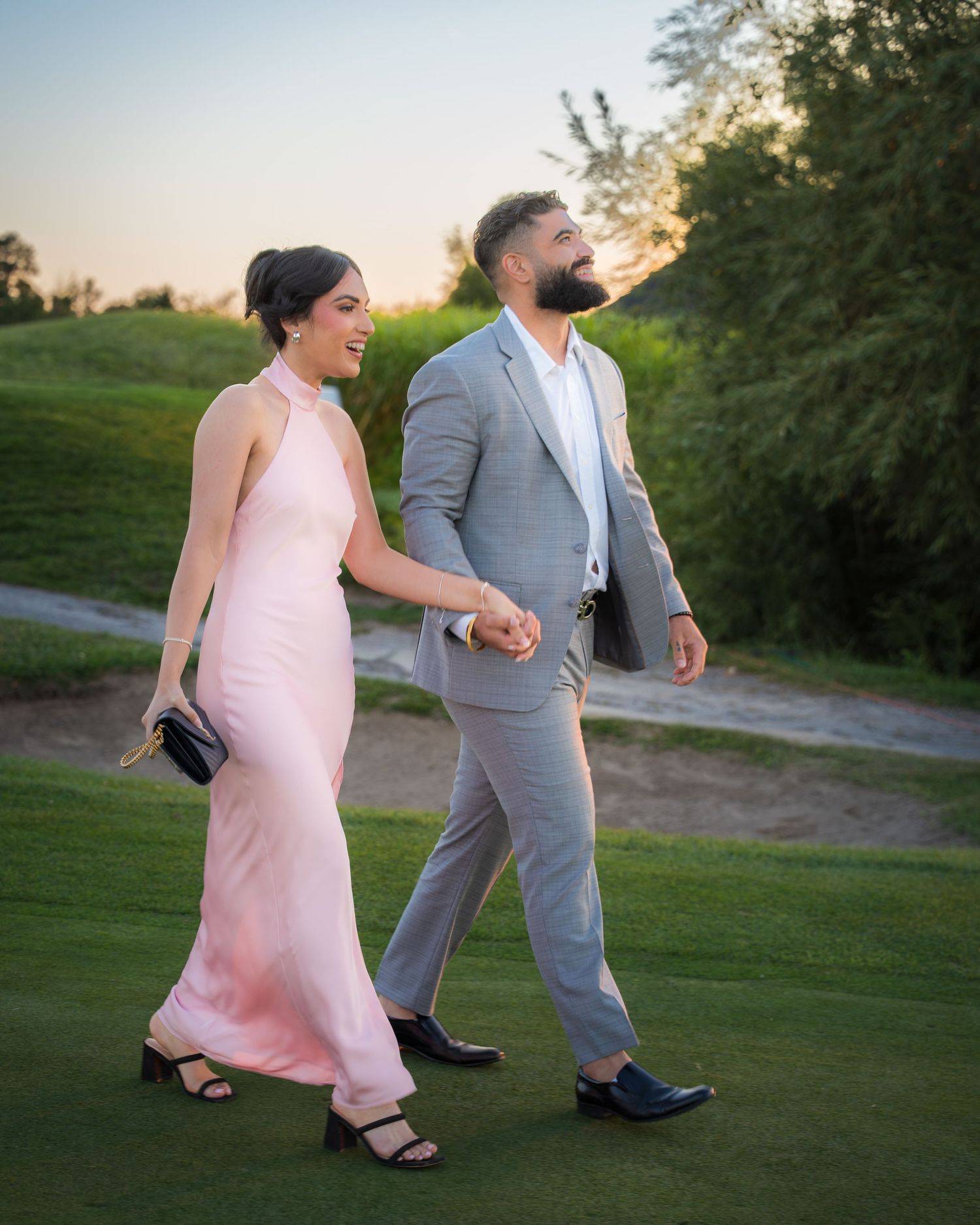Couple walking together on golf course path during sunset celebration.
