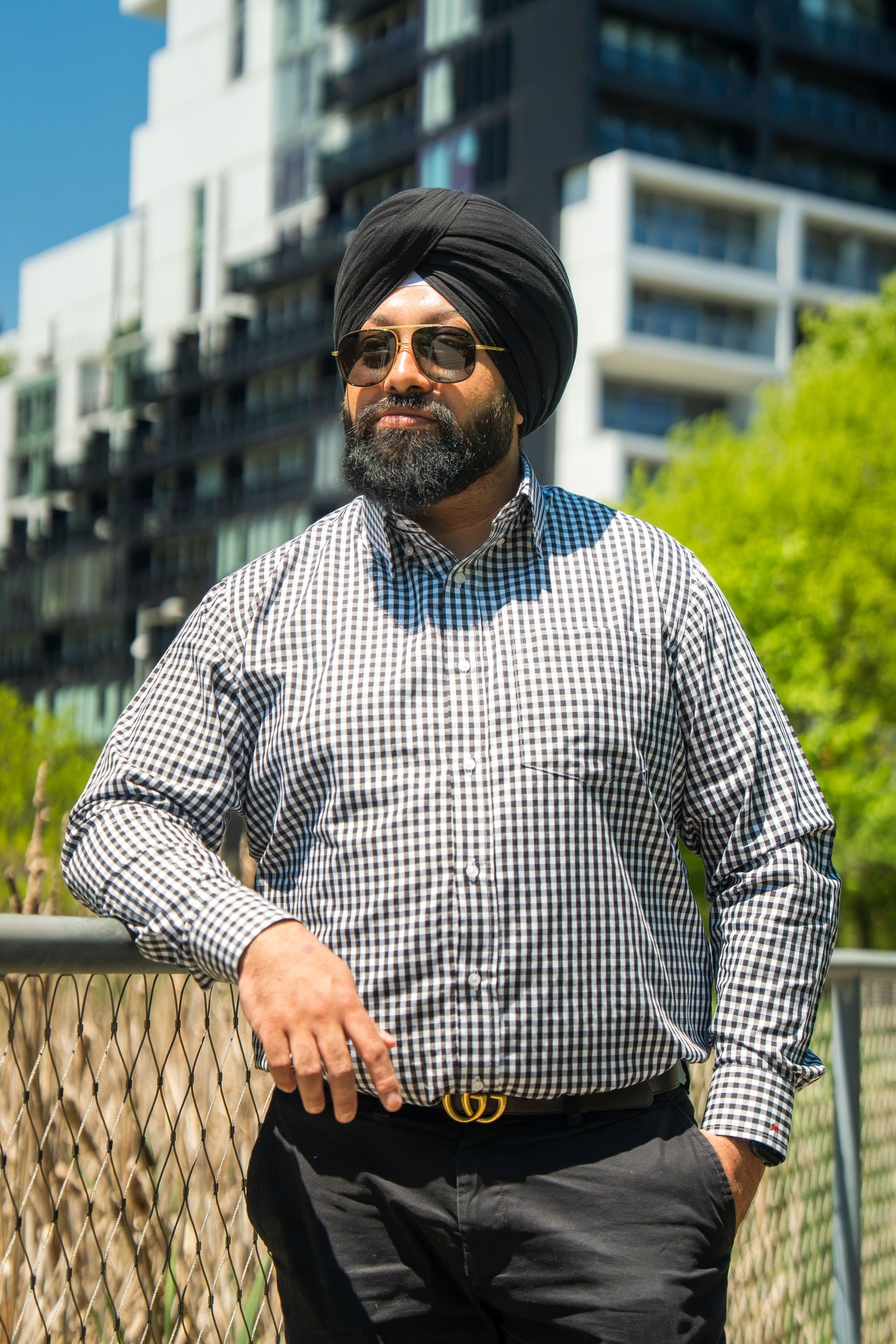 Bearded Sikh man wearing turban and sunglasses leaning on a railing outdoors on a sunny day.