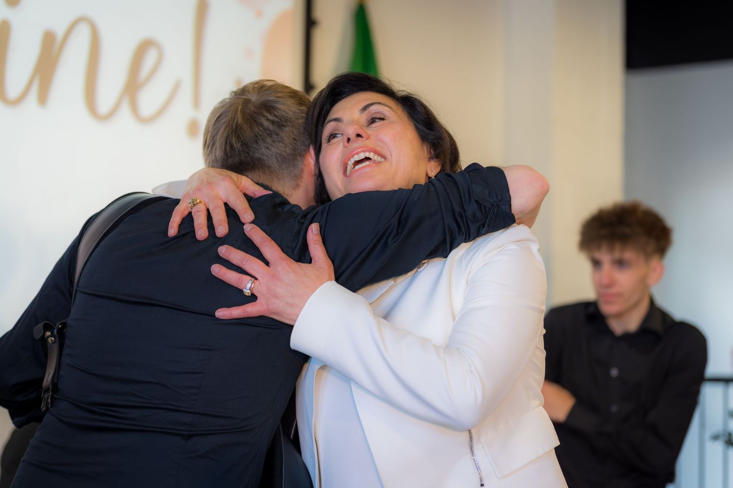 Two people sharing warm embrace at indoor event, smiling joyfully.