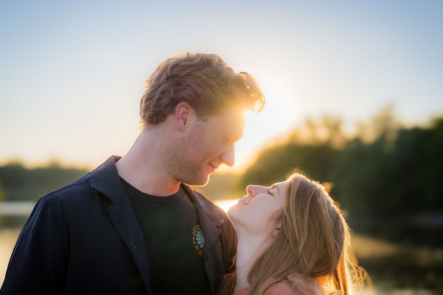 Romantic couple gazing at each other with a glowing sunset over a lake in background.
