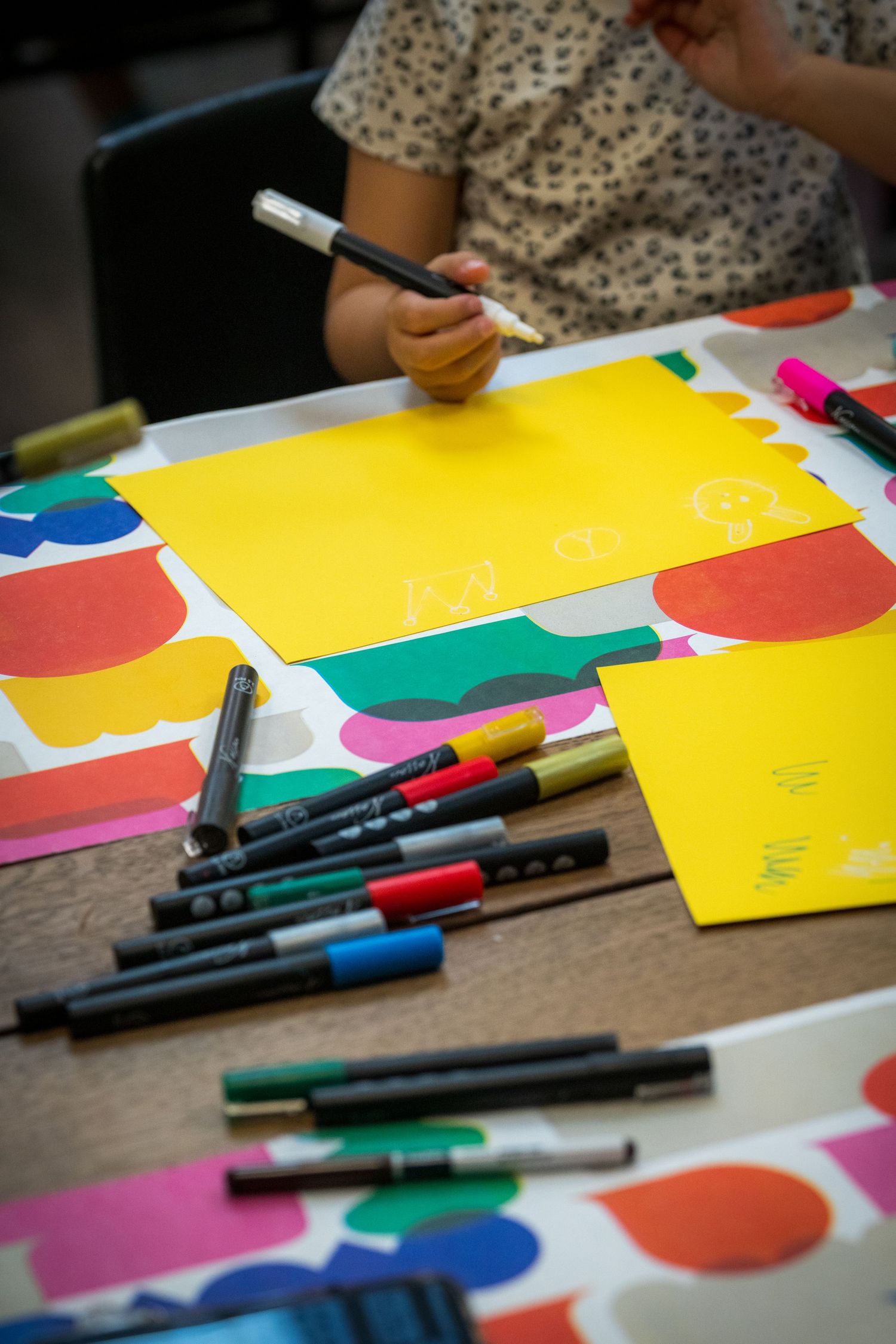 Colorful markers and bright paper sheets spread on a table during a children's art activity.