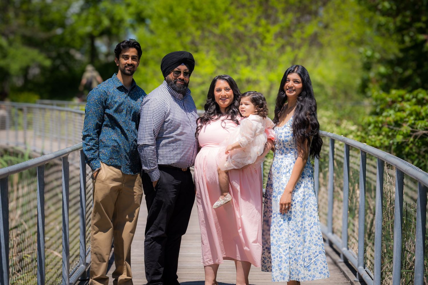 South Asian family of five posing together on a bridge in a lush green park.