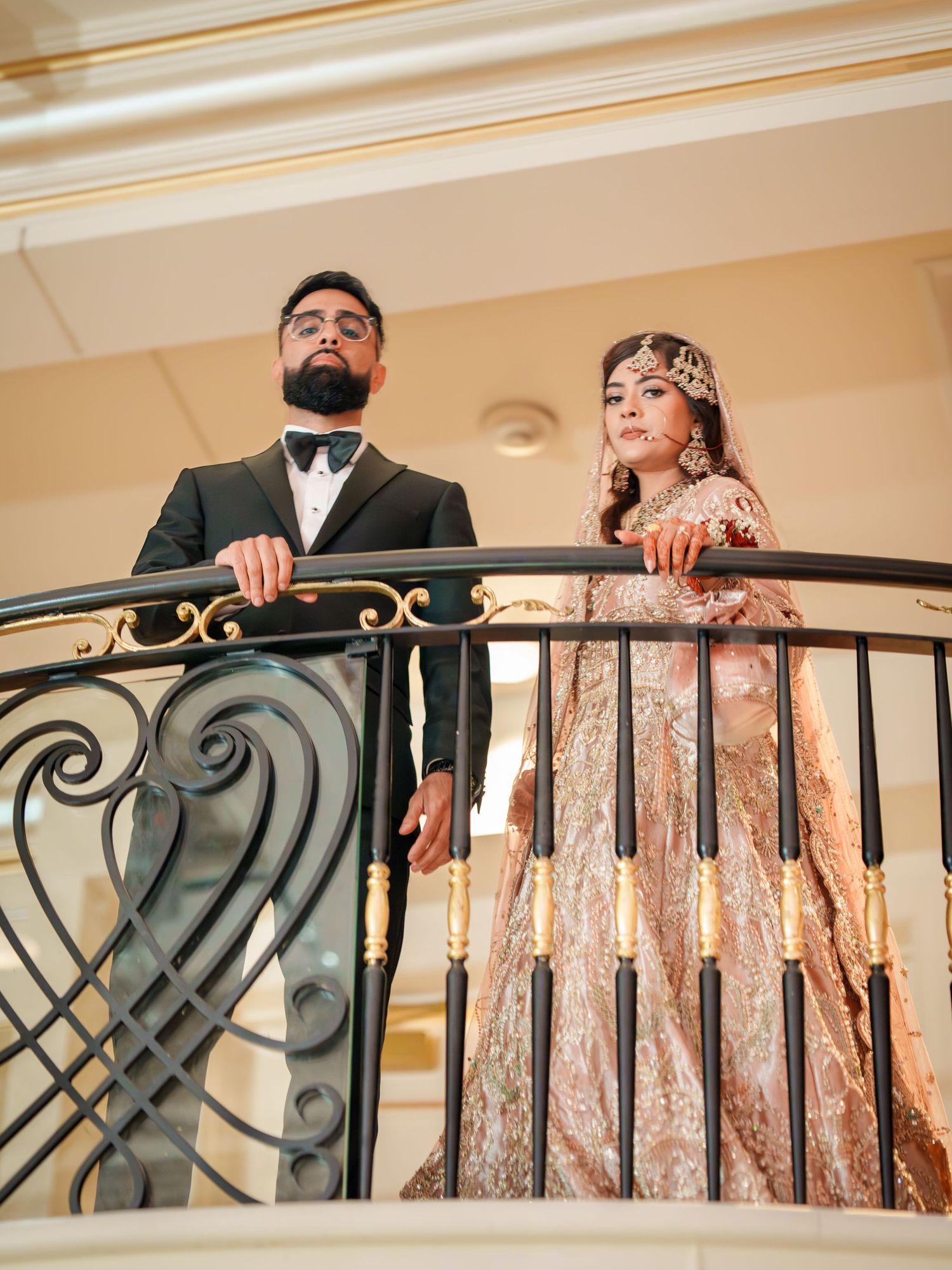 A couple in formal attire pose together on an elegant curved staircase with iron railings.