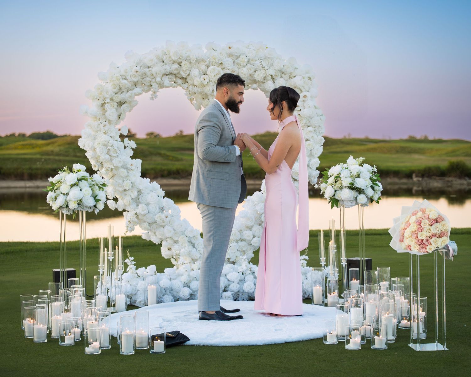 Beautiful proposal setup featuring white floral arches and glowing candles on a golf course.