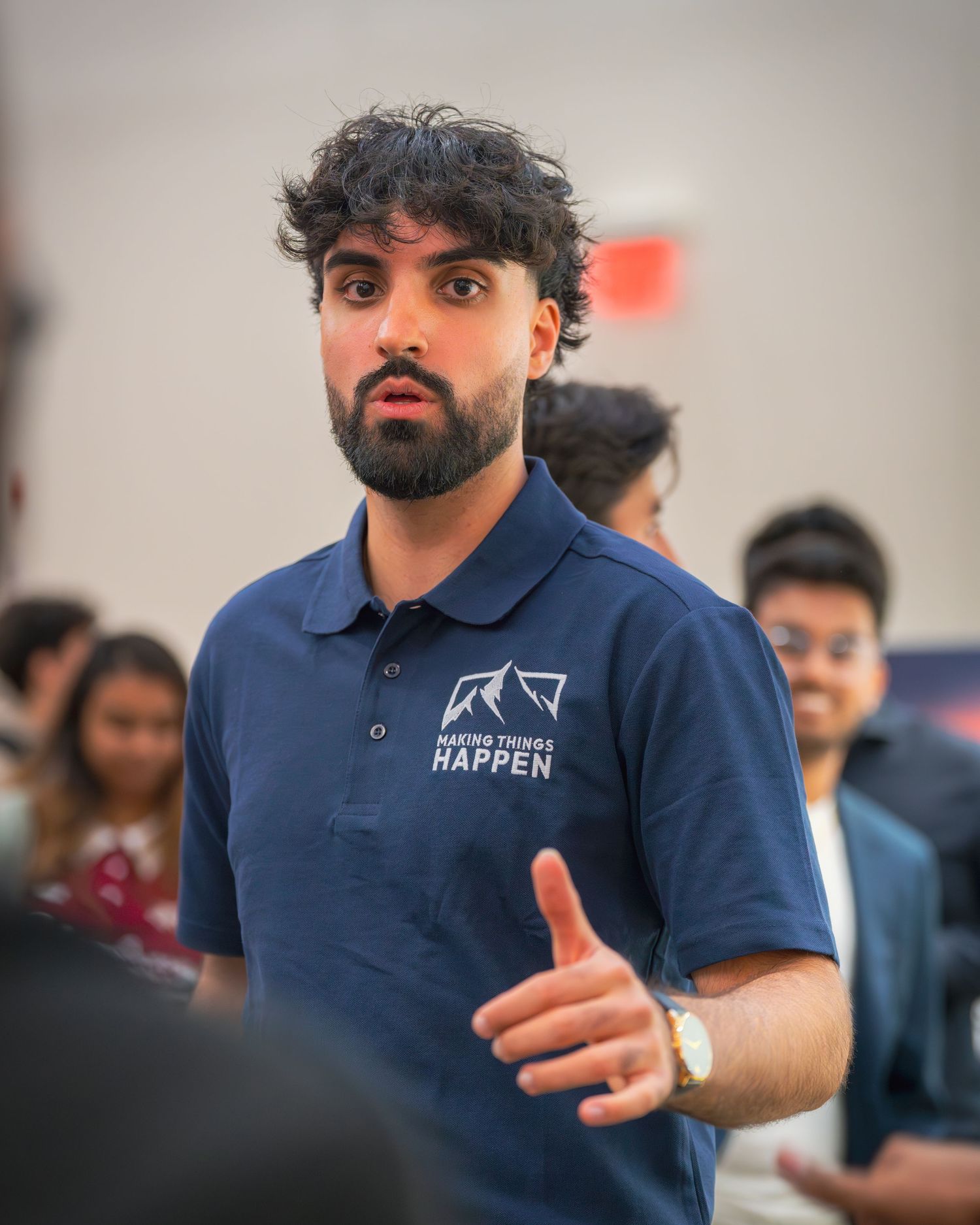 Speaker in a navy blue polo shirt with 'Making Things Happen' logo gesturing during a presentation.