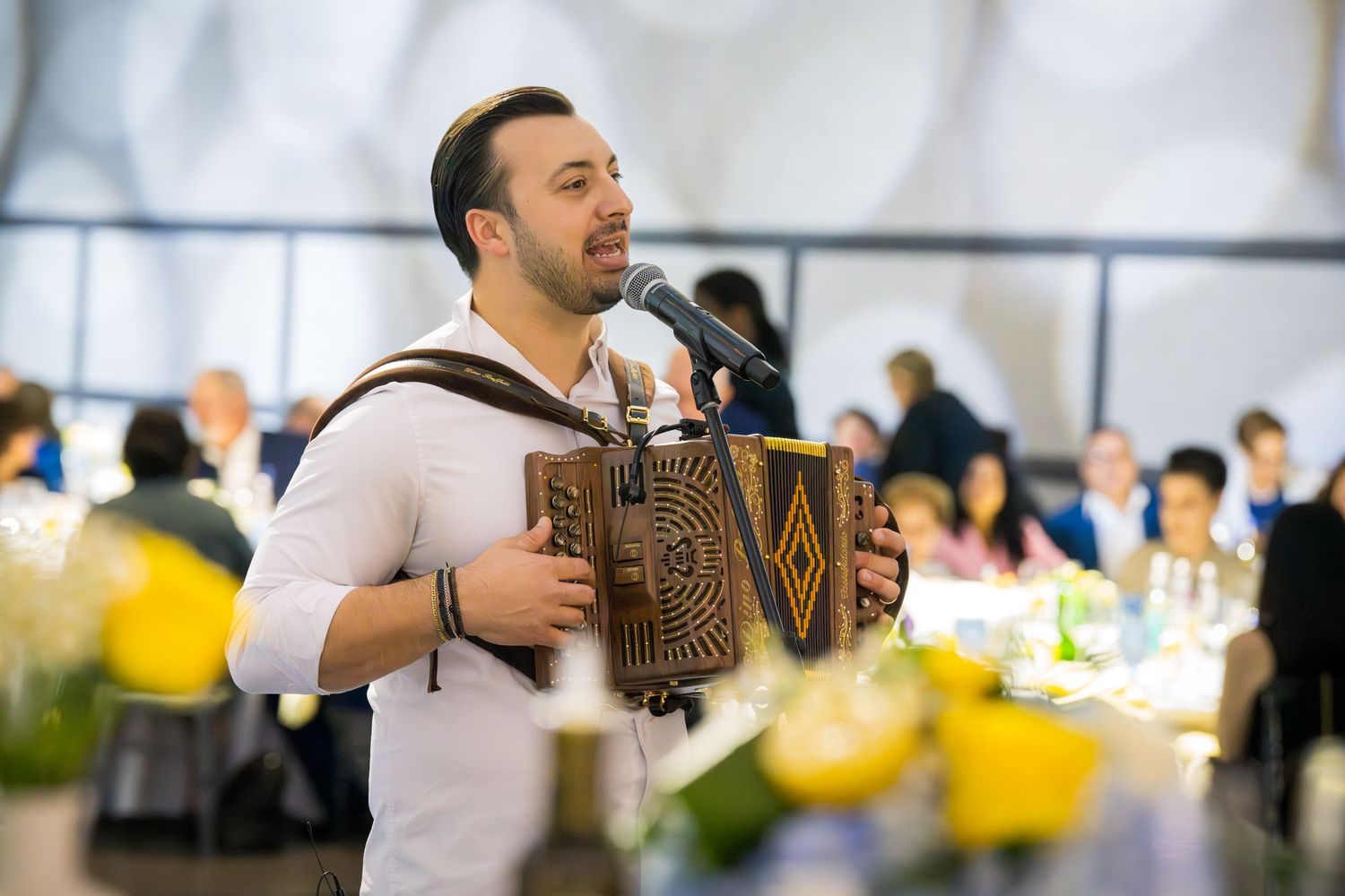 Male musician playing accordion and singing into microphone at a wedding reception.