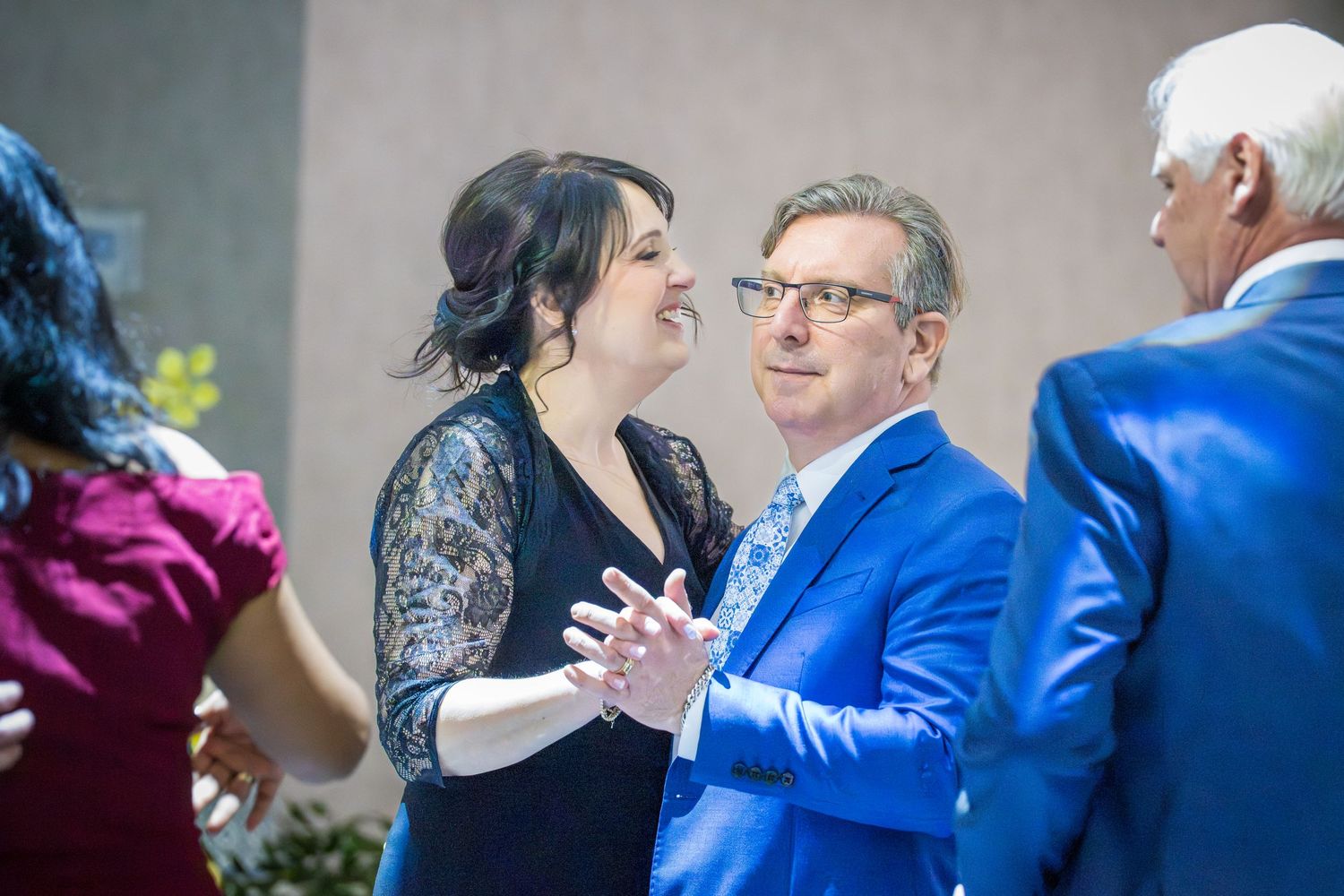 A woman in black lace and a man in blue suit share a joyful conversation at a formal event.