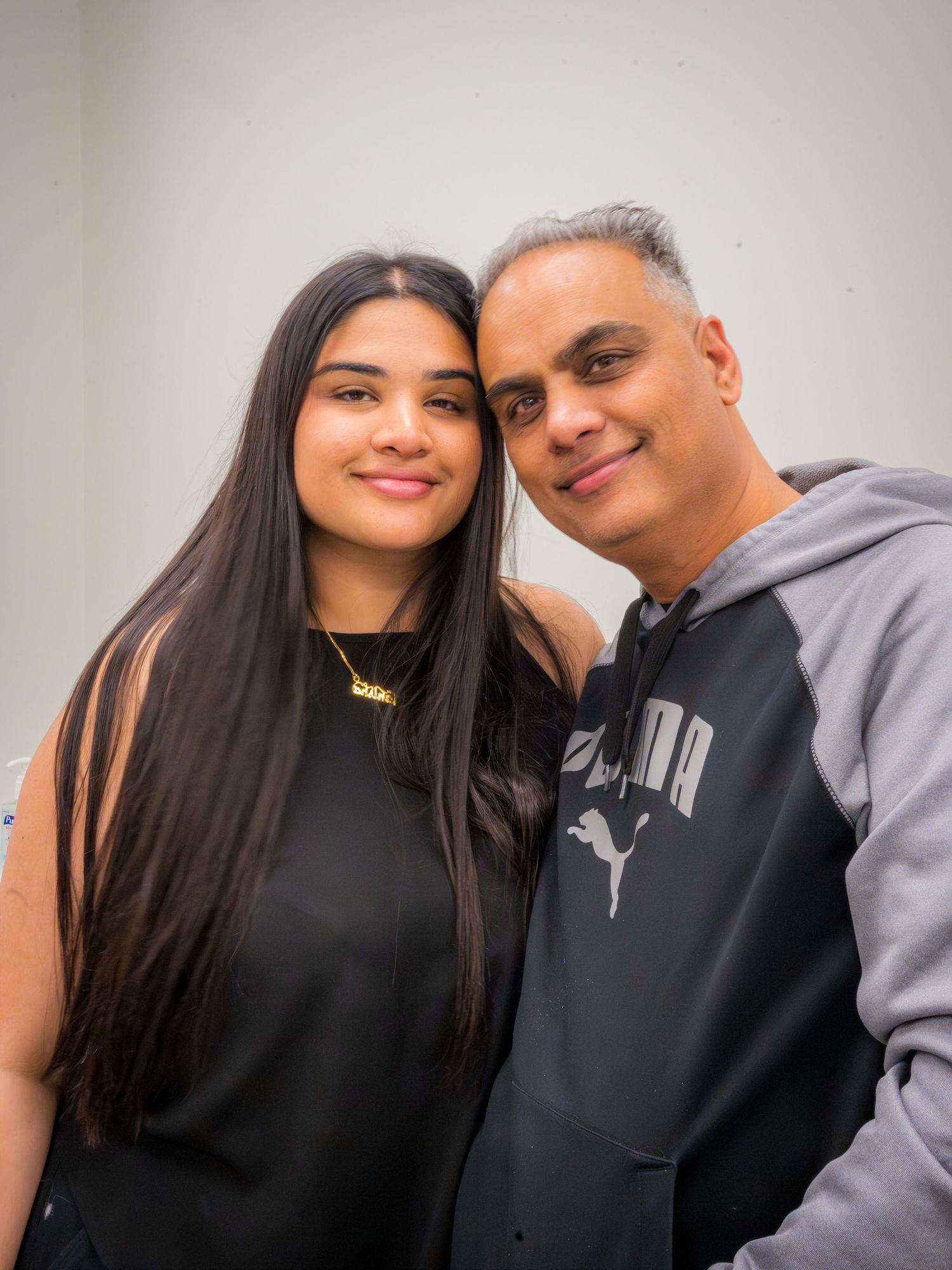 A young woman and older man smile together posing for a photo wearing casual Puma hoodies.