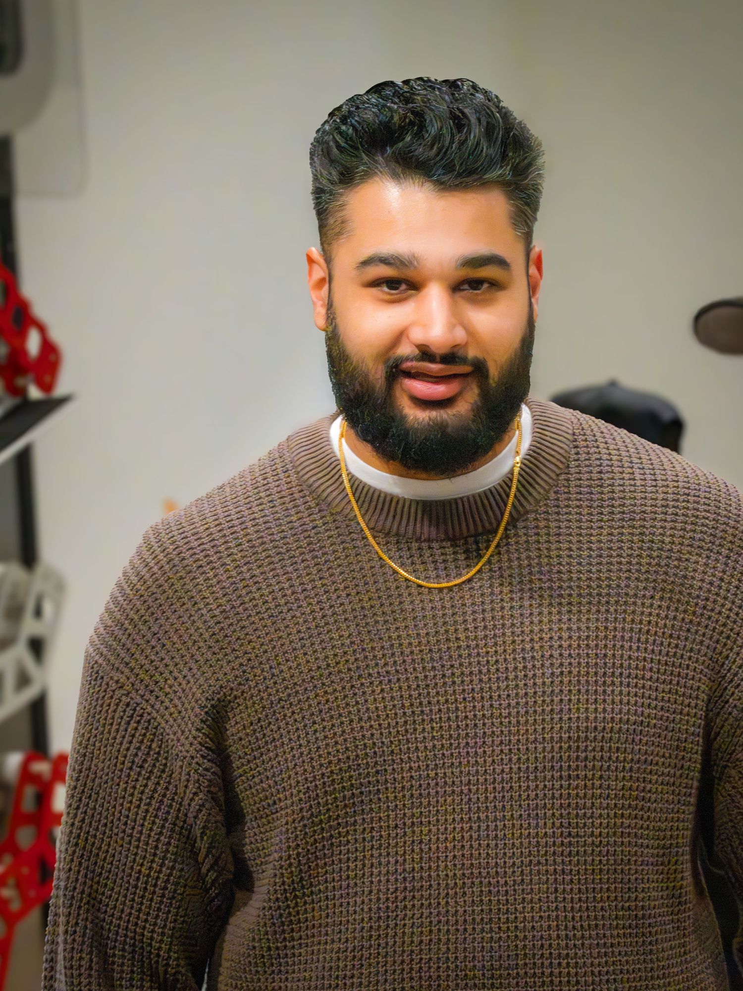 Bearded man in brown waffle knit sweater and gold chain smiling indoors.