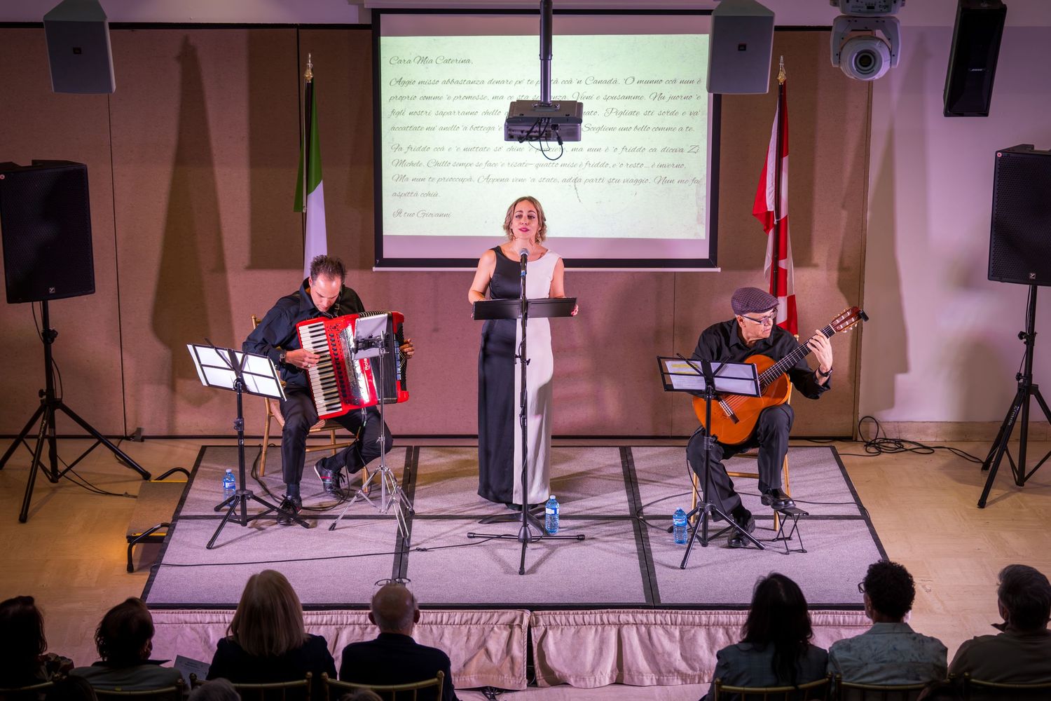 Three musicians perform on stage with accordion and guitar, a woman singing at a microphone between them.