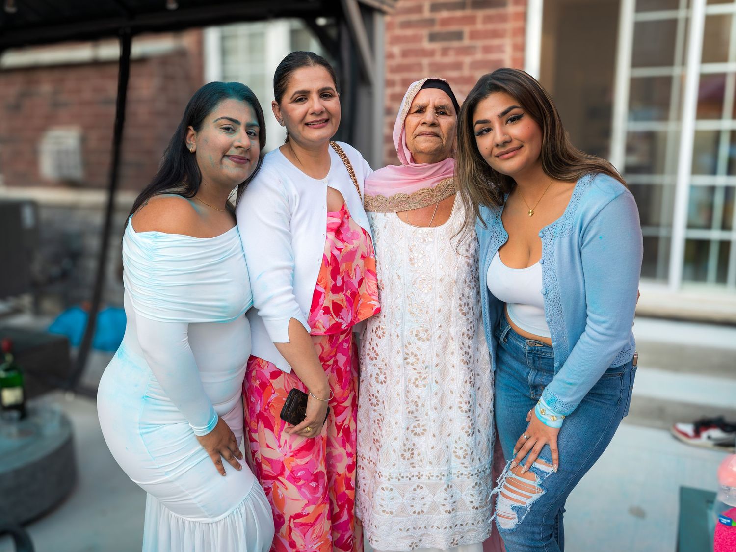 Four women posing together outdoors at a gender reveal party, some covered in blue powder.