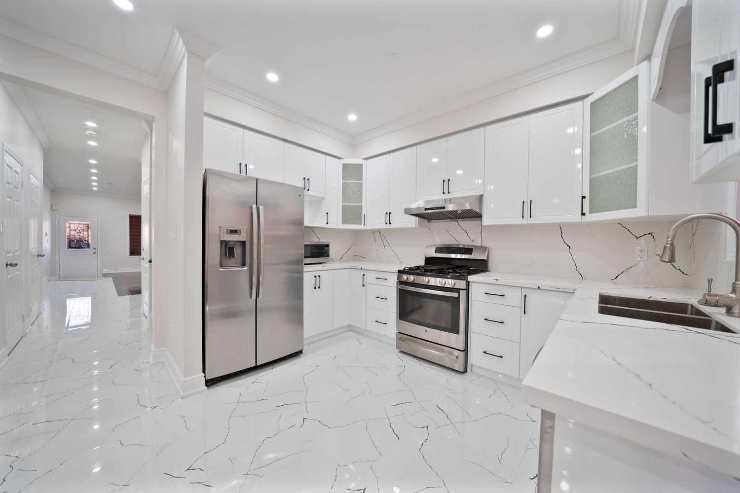 Modern white kitchen interior with sleek cabinets, marble countertops, and recessed lighting showcases contemporary design.