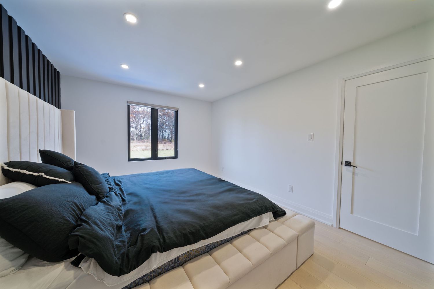 Modern bedroom with black bedding, white platform bed frame, recessed lighting and white walls.