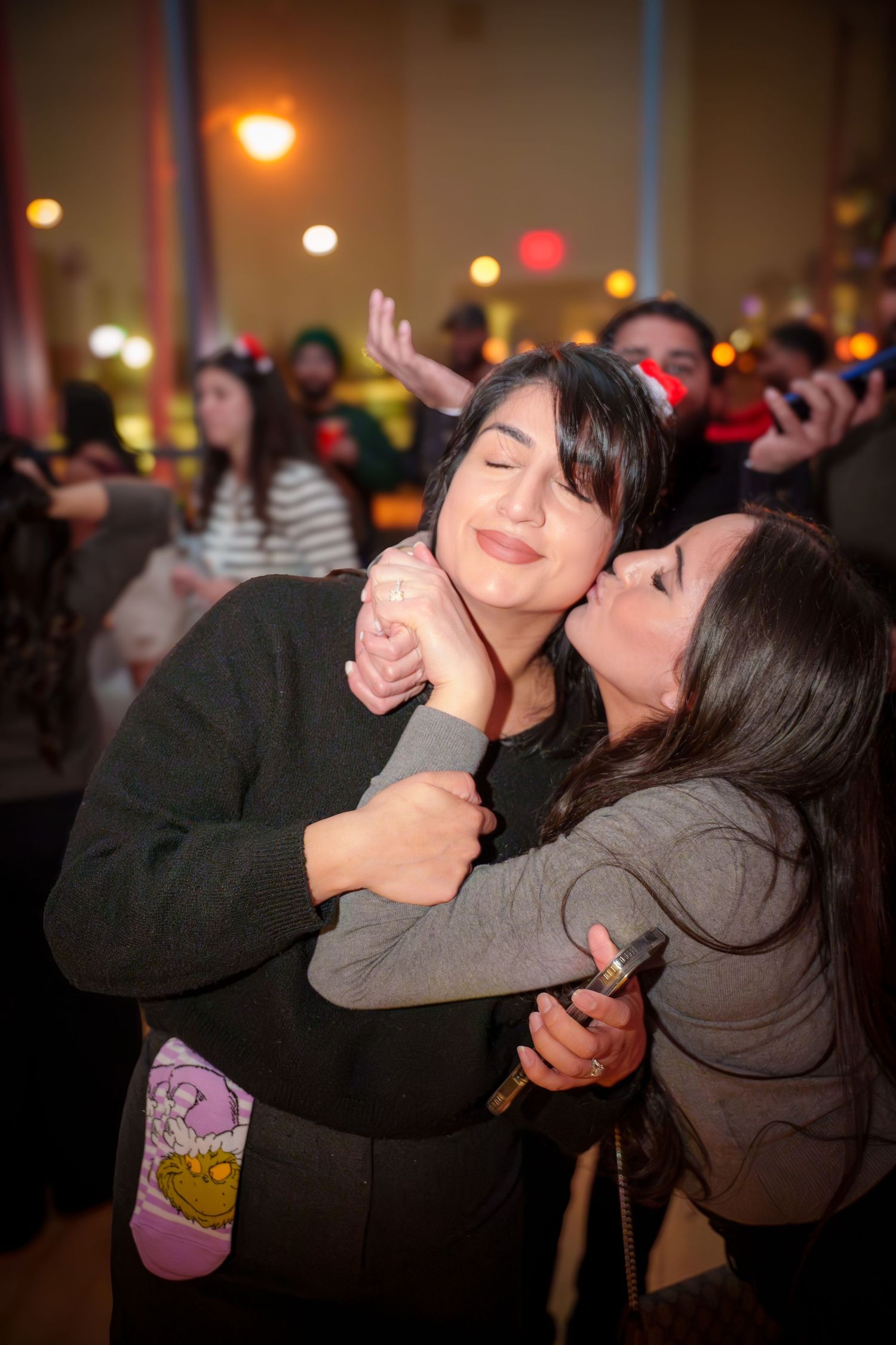 Two friends share an affectionate moment at a dimly lit party.