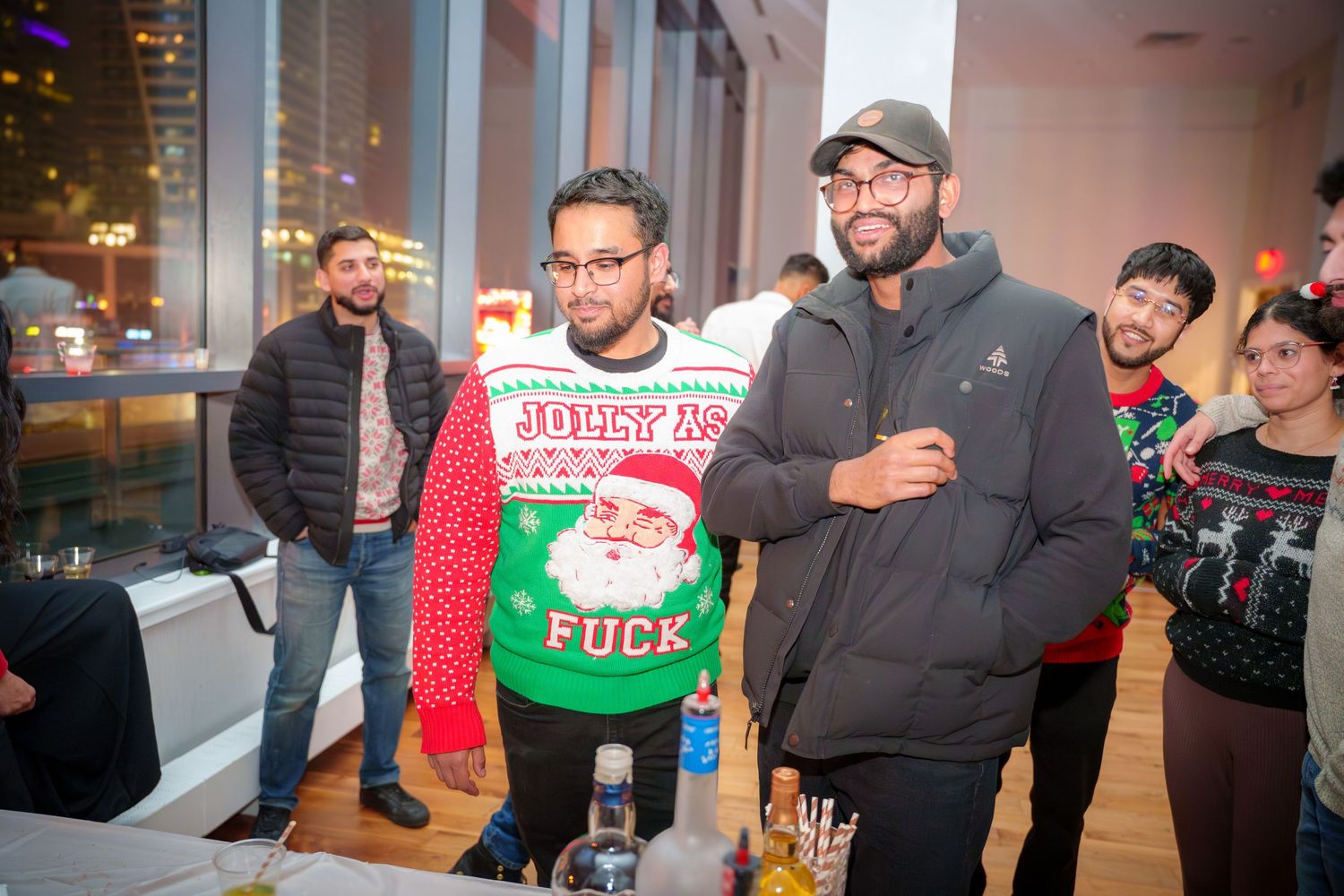 Friends wearing festive holiday sweaters at indoor party gathering.