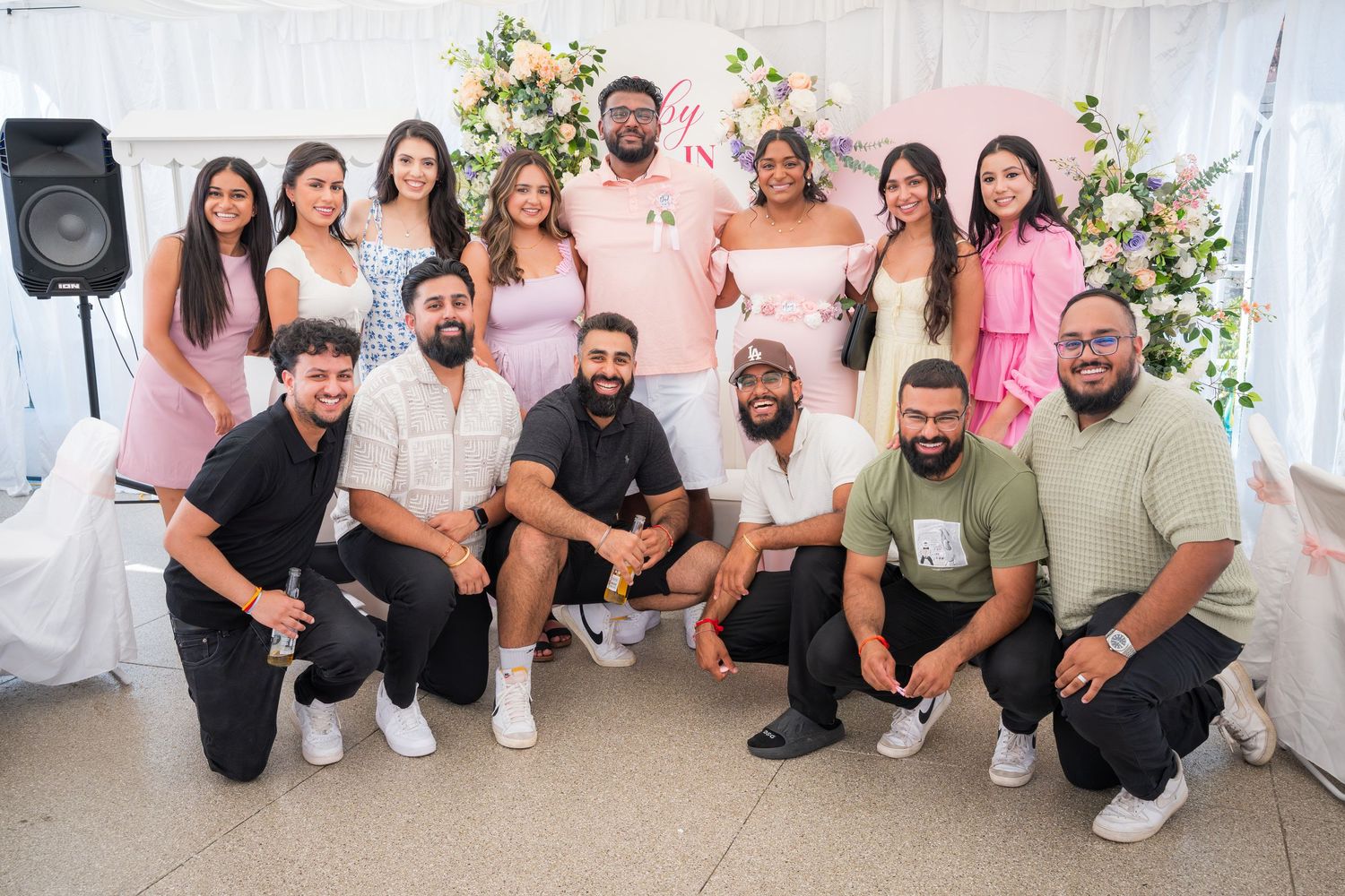 Large group photo of celebration attendees in coordinated pink and white outfits.