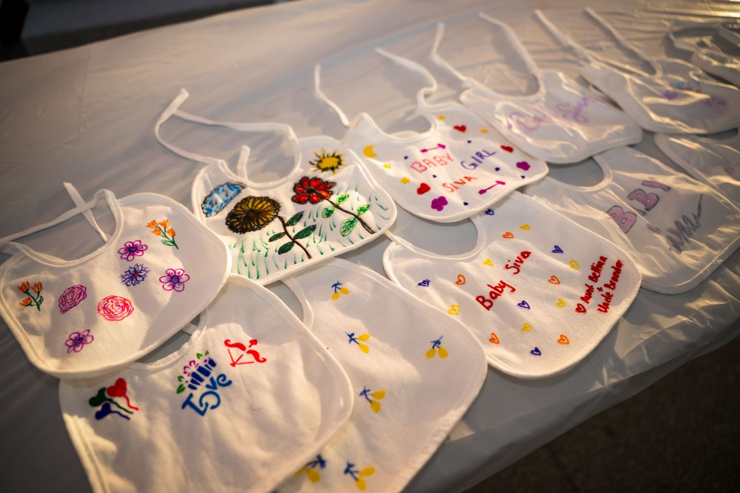 Multiple white baby bibs with handmade decorations displayed on a surface.