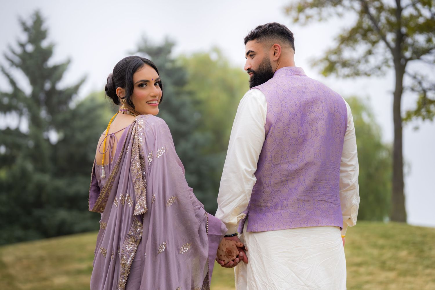 Couple in coordinated South Asian attire walking together on a hillside during golden hour.