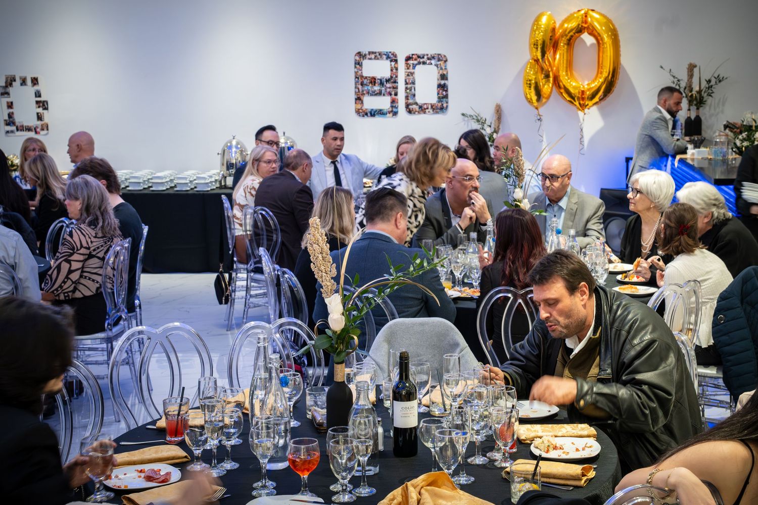 Group of people mingling at an elegant event with gold balloon decorations and dark backdrop.
